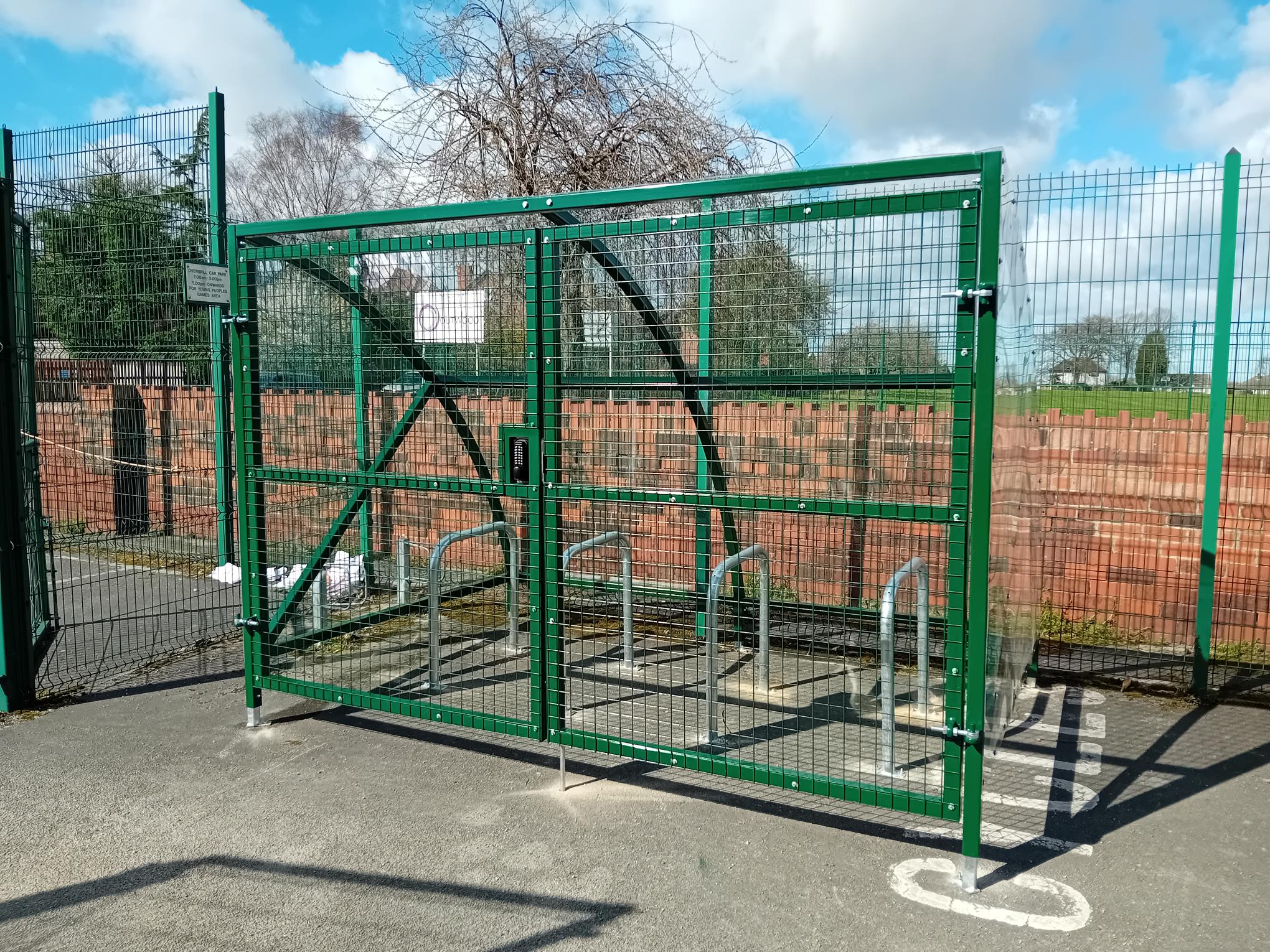 Green metal bike storage cage with clear sky and trees