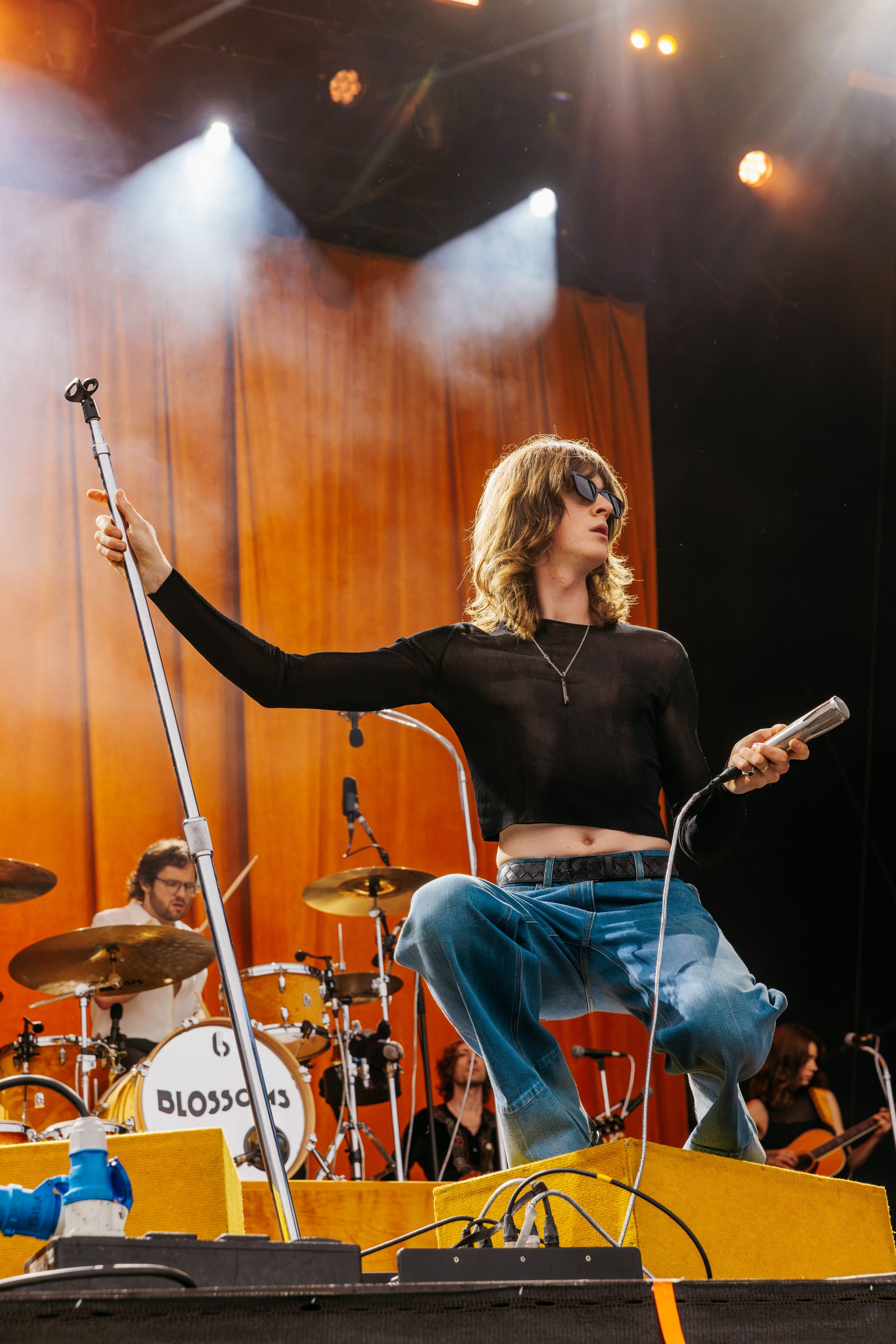 Singer in sunglasses on stage with band, orange backdrop