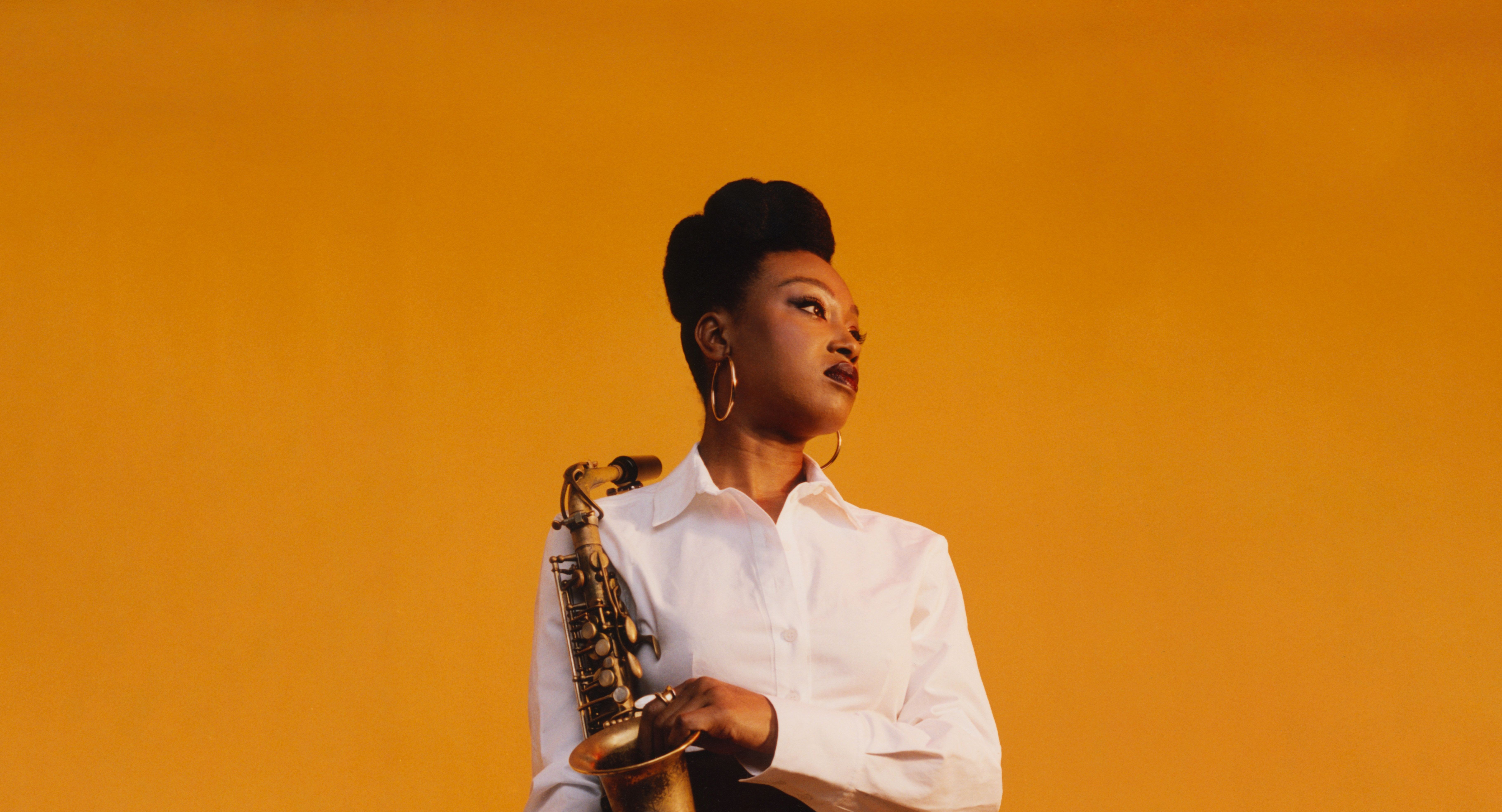 Musician holding saxophone against a warm amber background