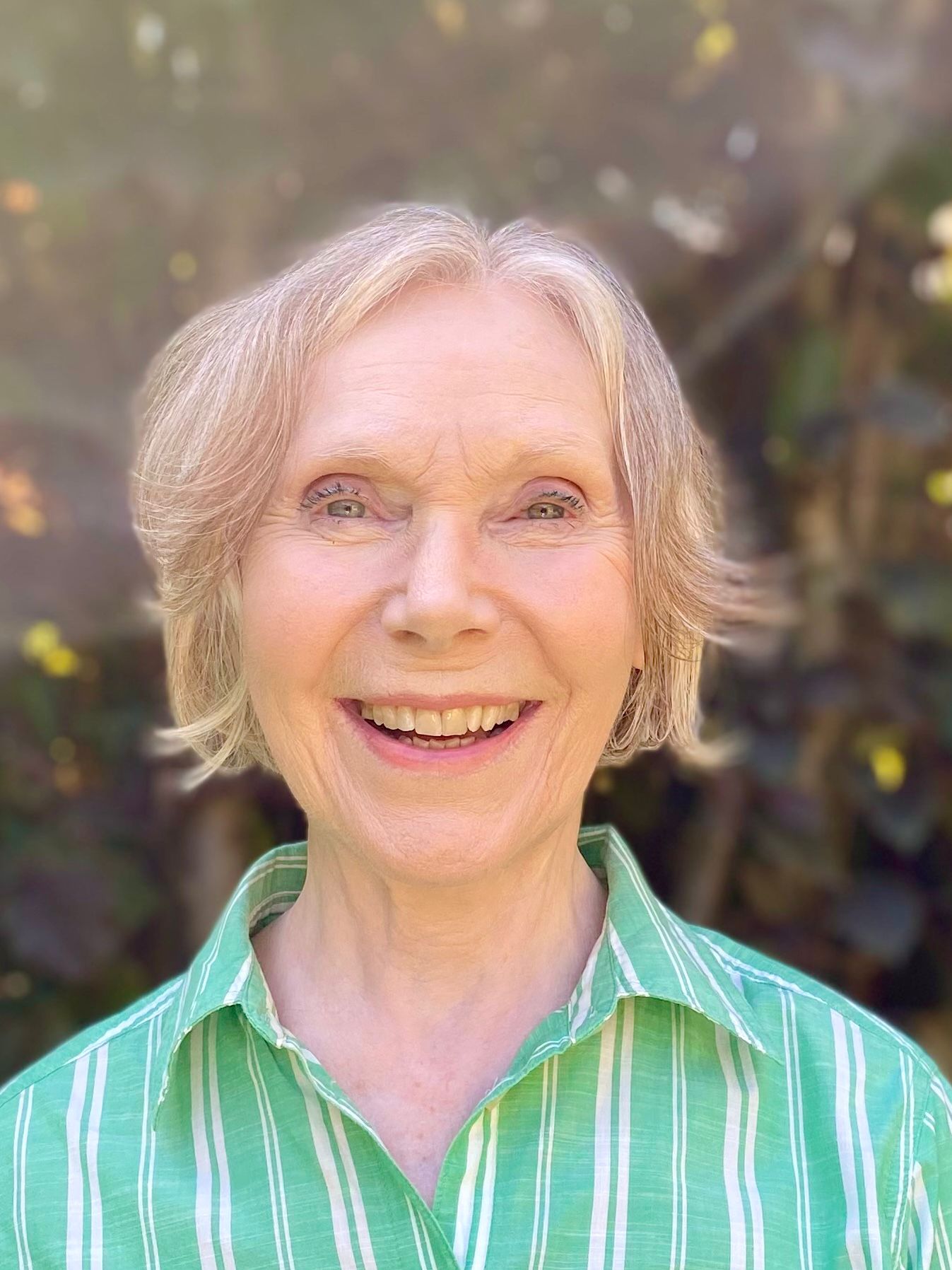 Elderly woman with short grey hair smiling in a garden setting