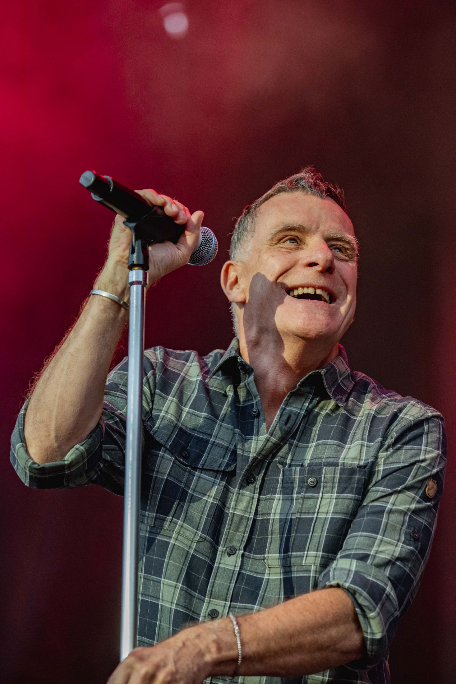 Smiling man in checkered shirt singing on stage with red lighting