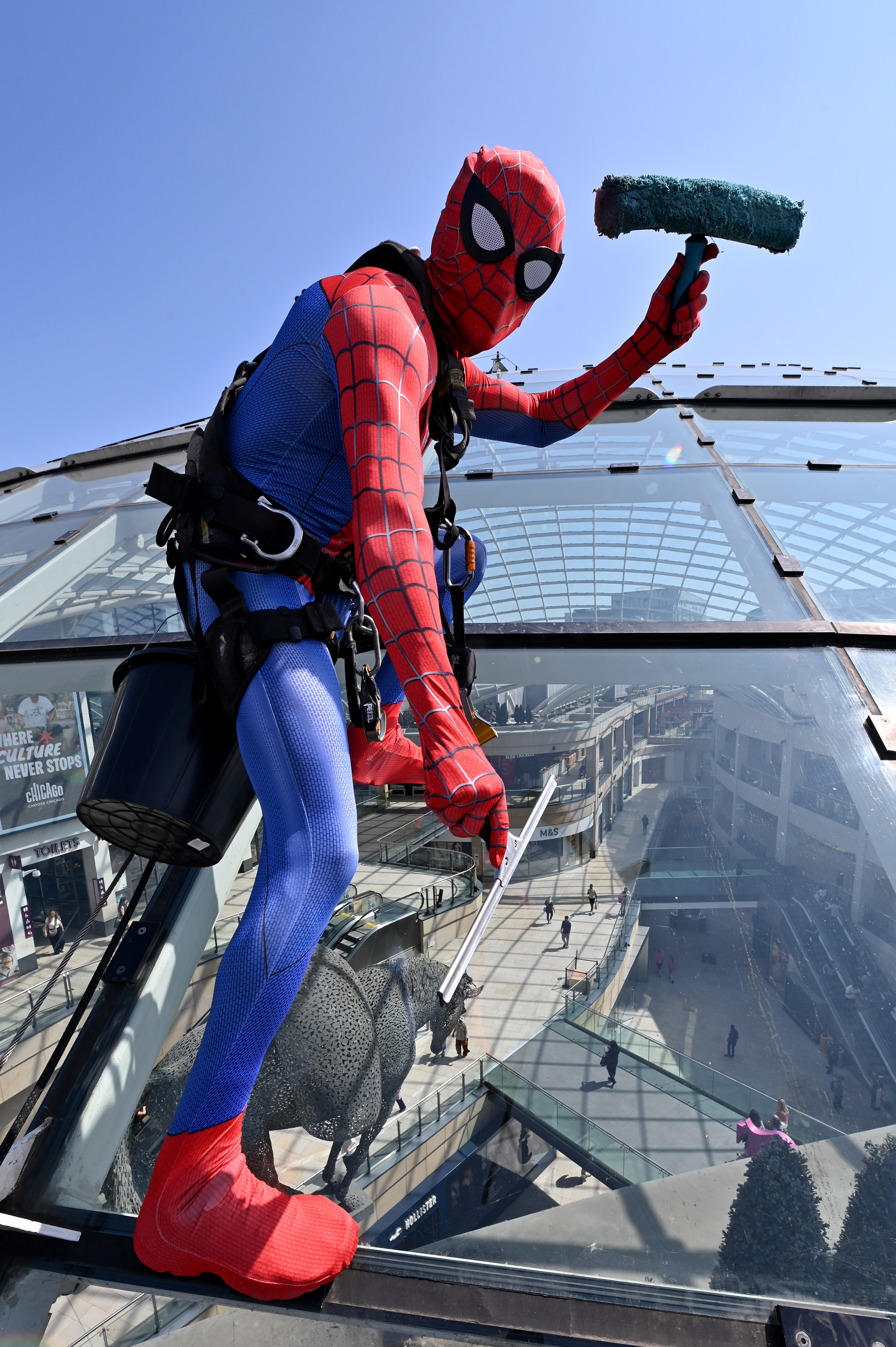 Person in superhero costume cleaning large glass roof in city centre