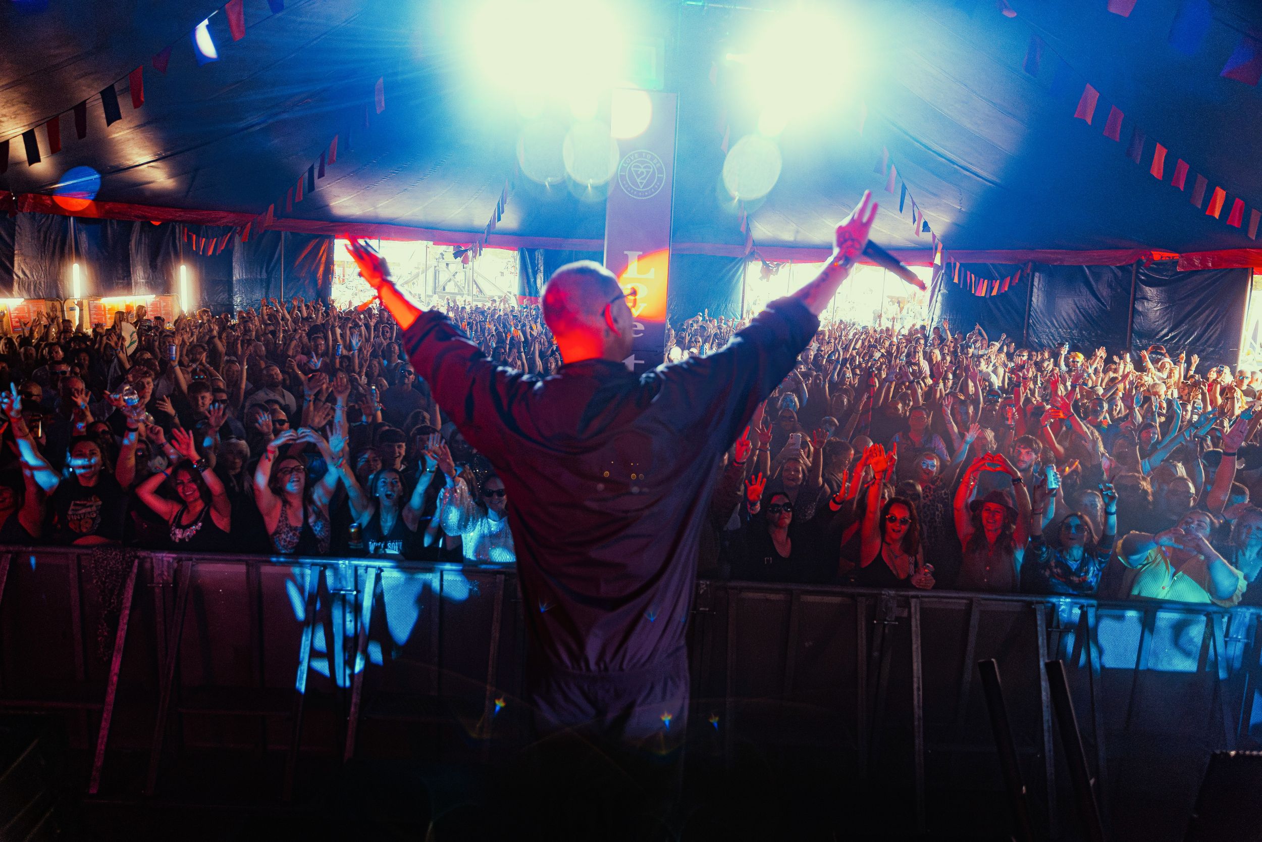 Musician on stage with cheering crowd in illuminated tent