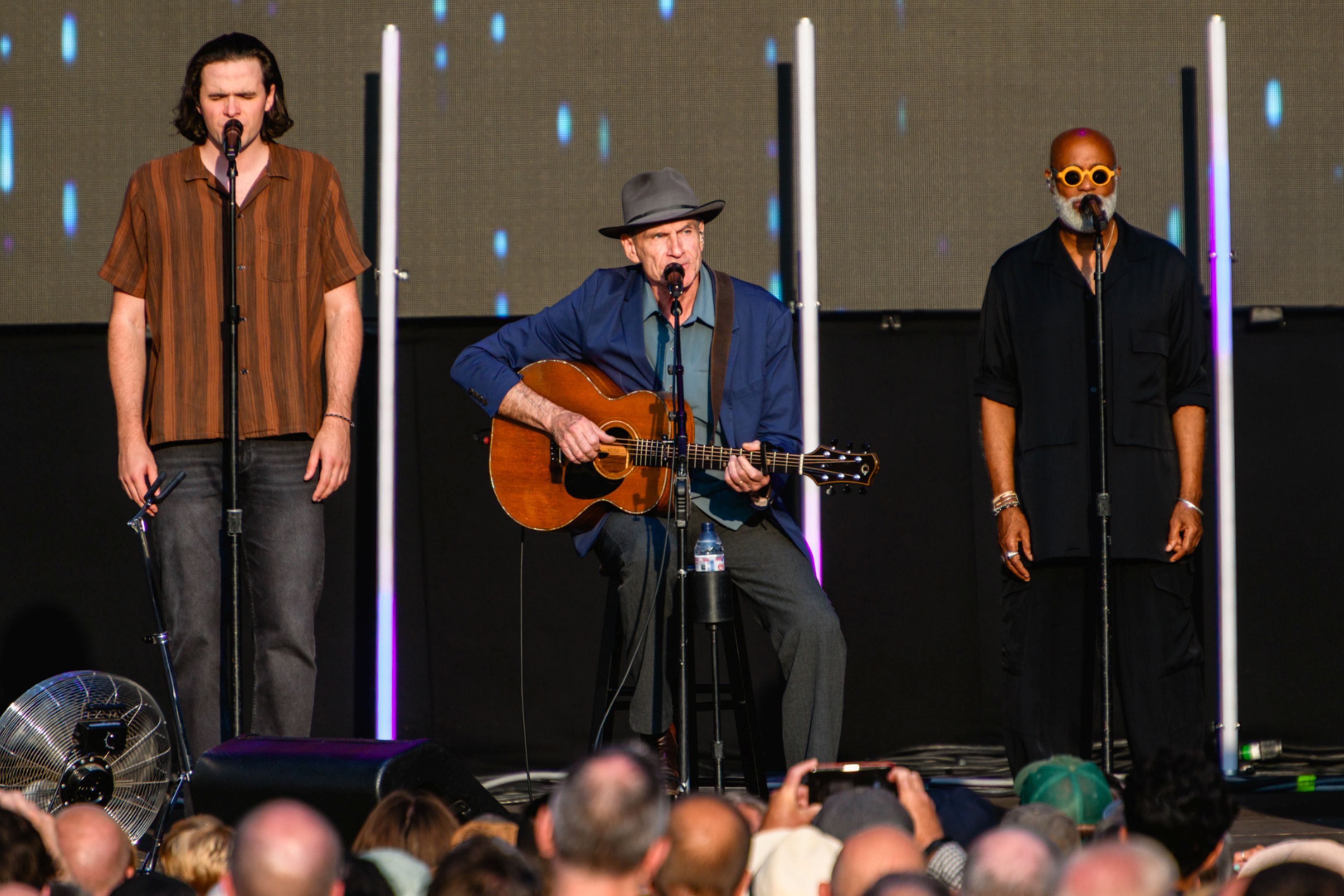Three musicians performing on stage, one playing acoustic guitar