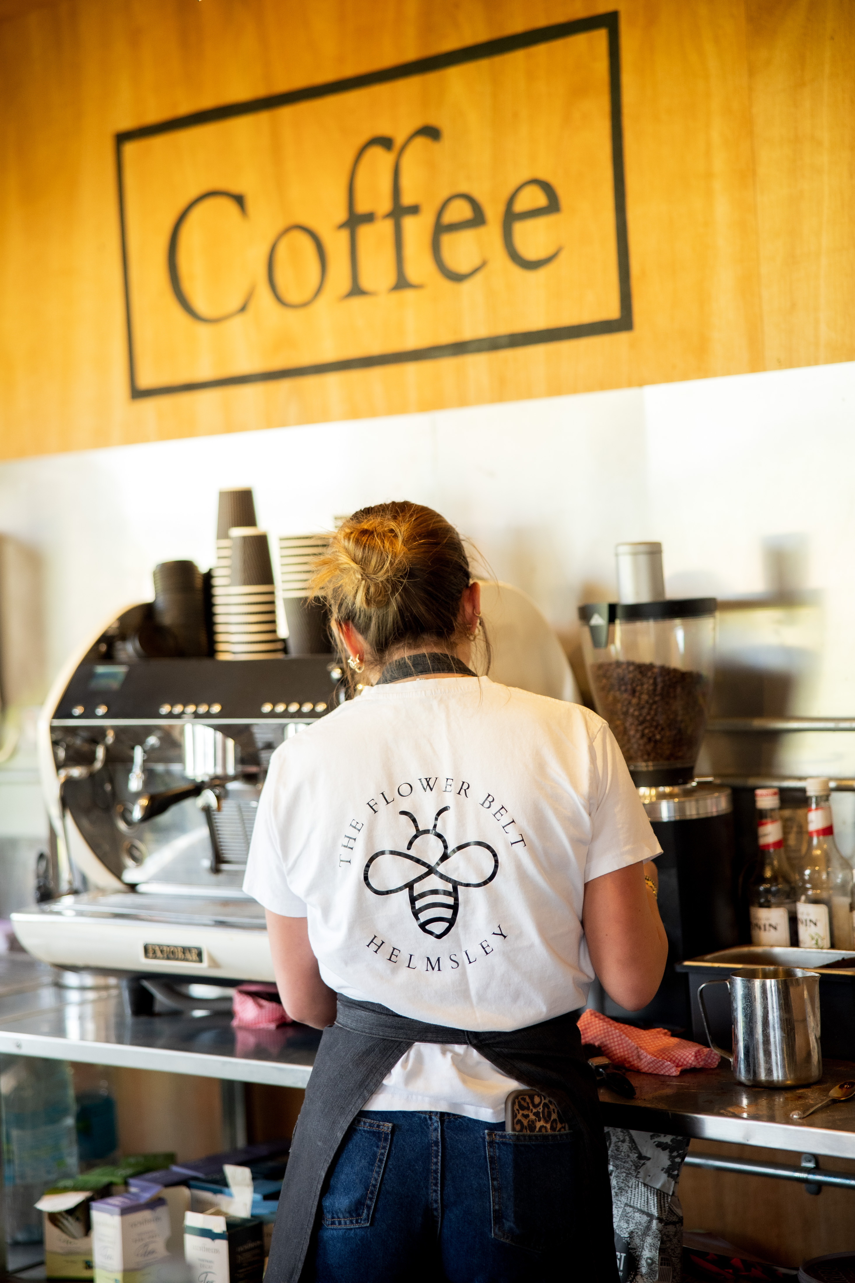 Barista in Helmsley cafe wearing bee logo shirt preparing coffee