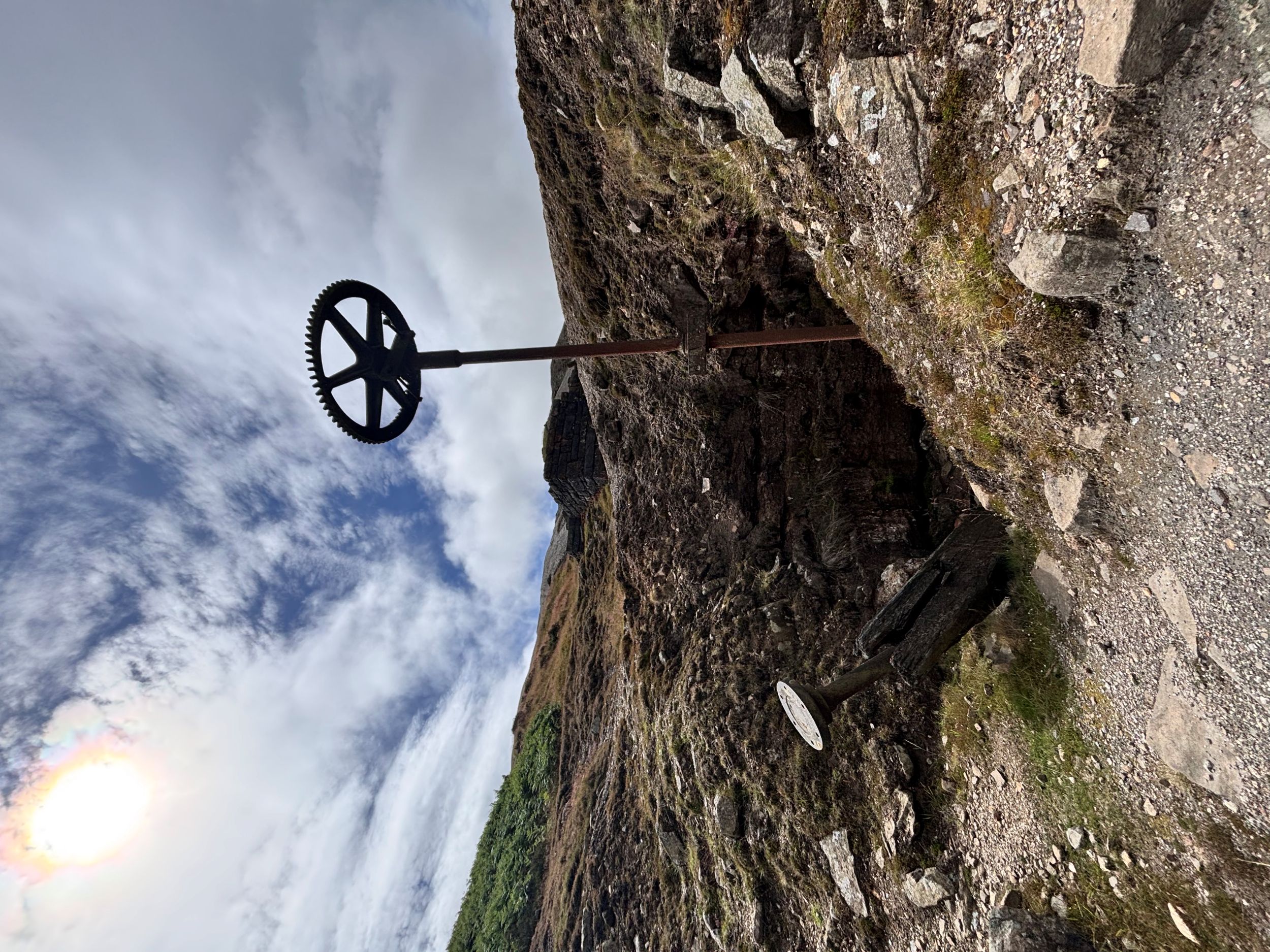 Old mining wheel on rocky hillside under cloudy sky