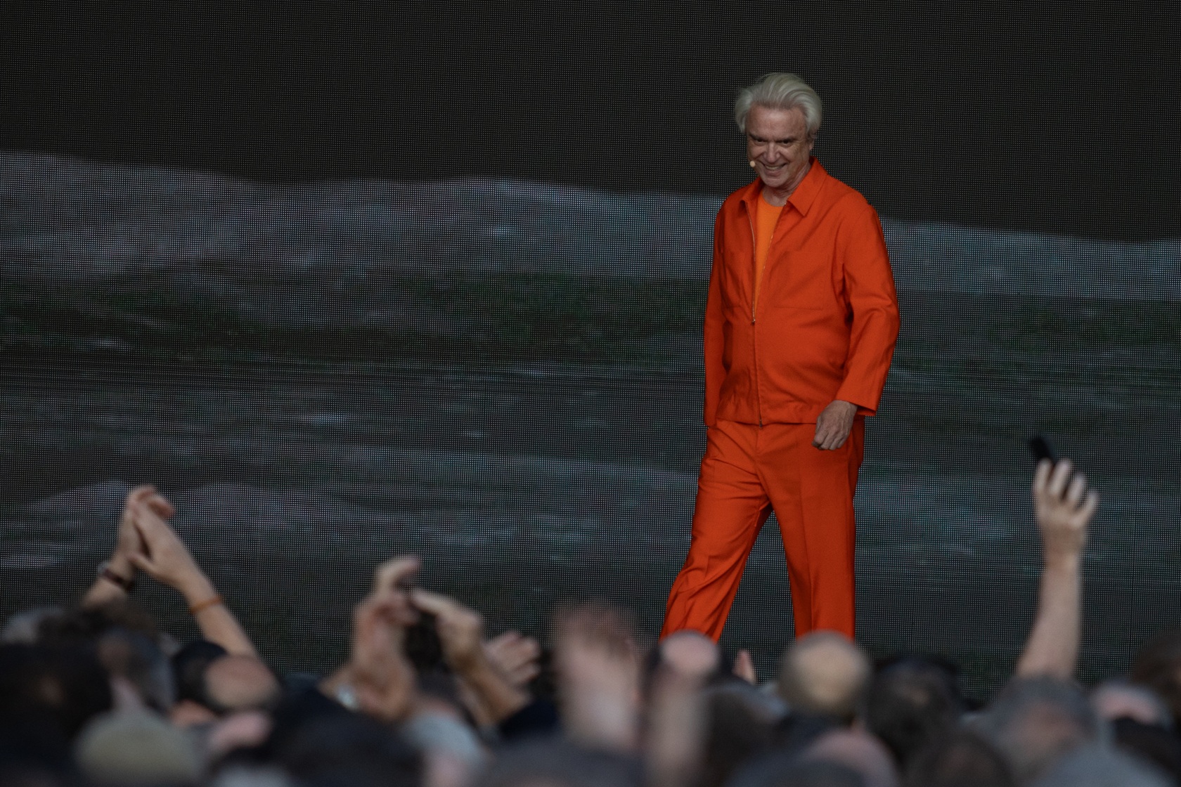 Elderly man in an orange suit on stage with audience clapping