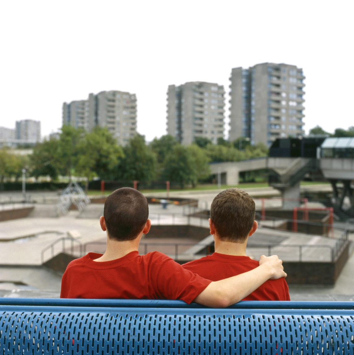 Two people in red shirts sitting on a bench overlooking urban park