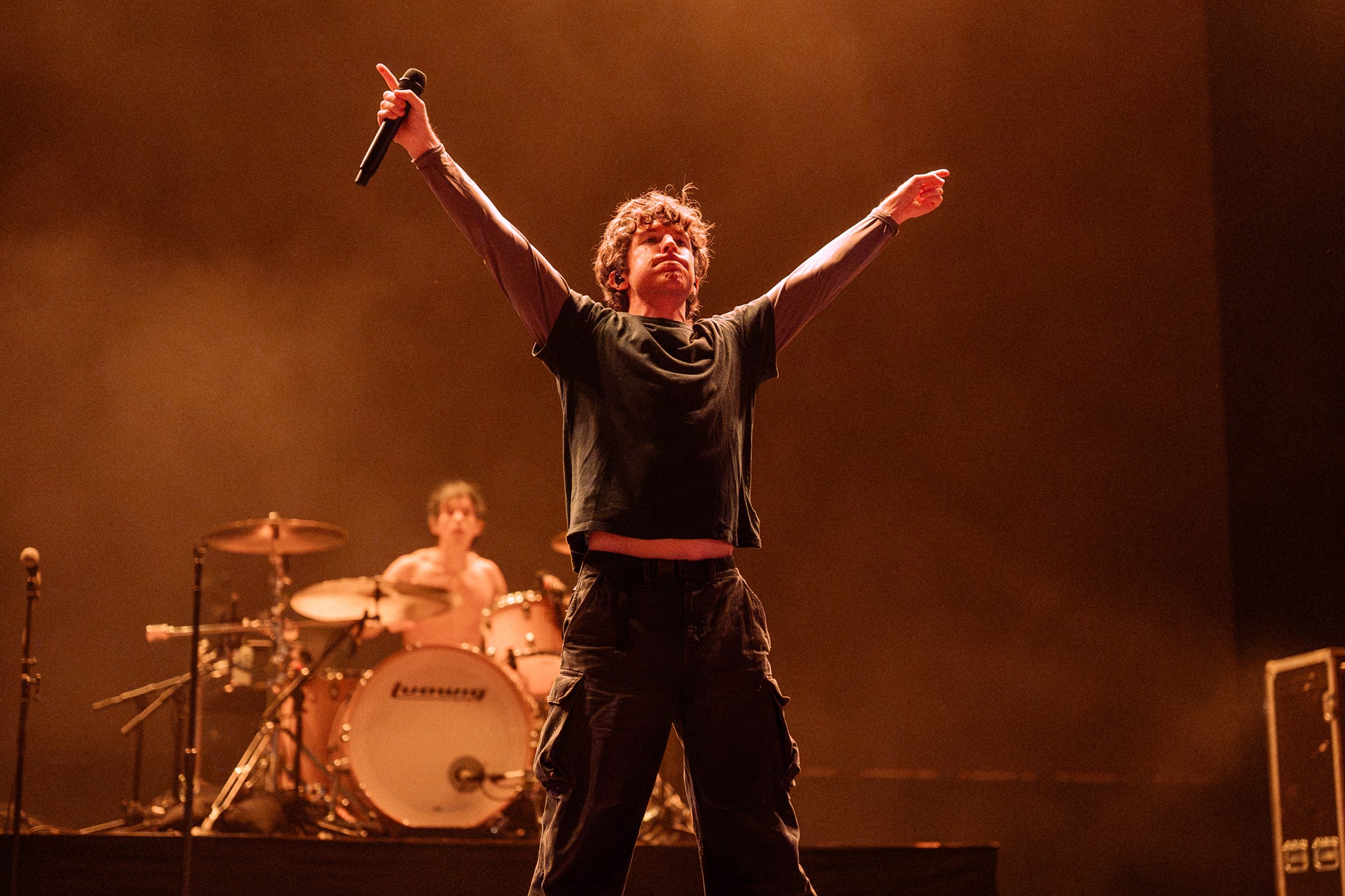 Musician on stage with arms raised, drummer in background