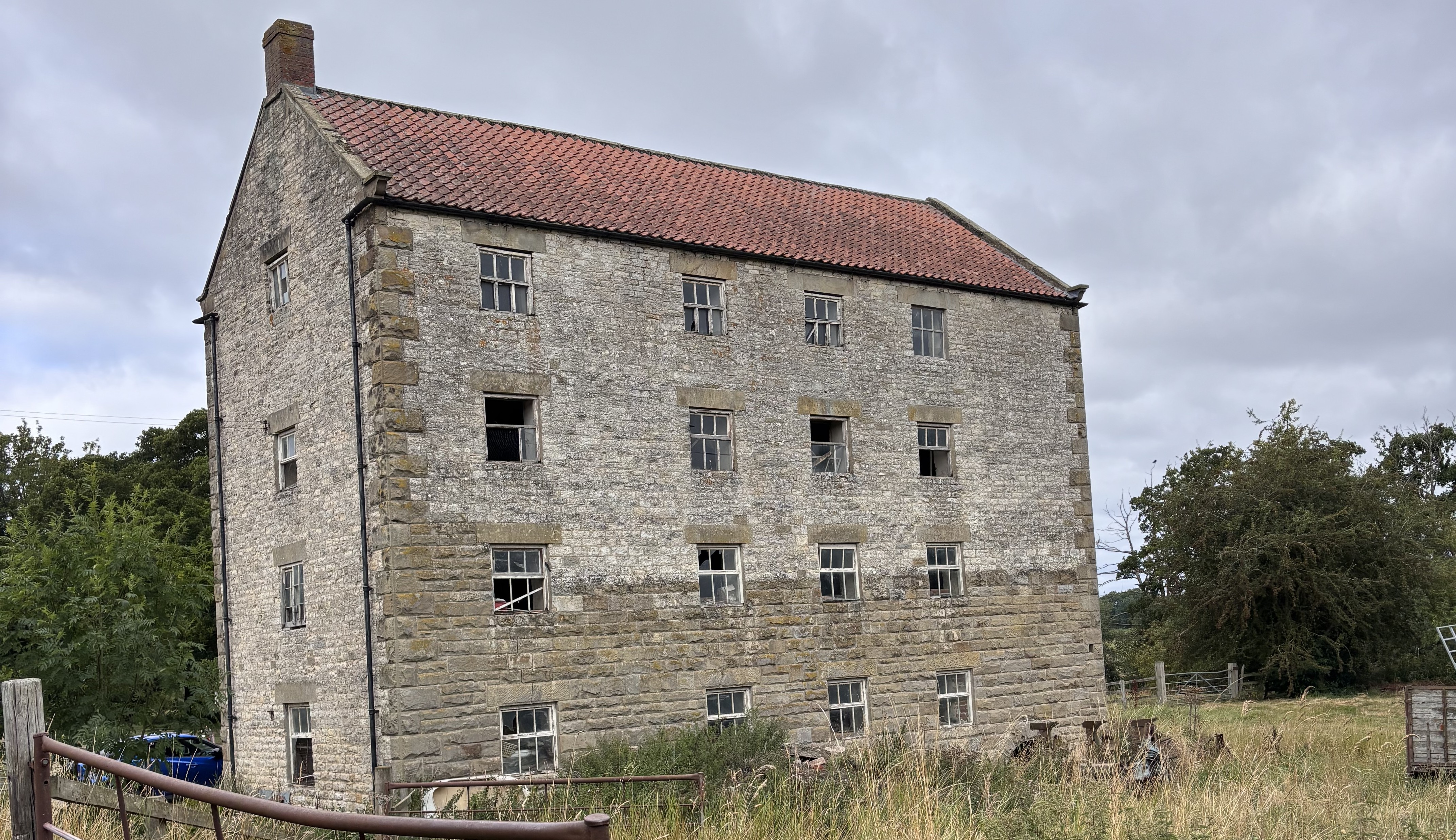 Historic stone mill building with red-tiled roof in countryside