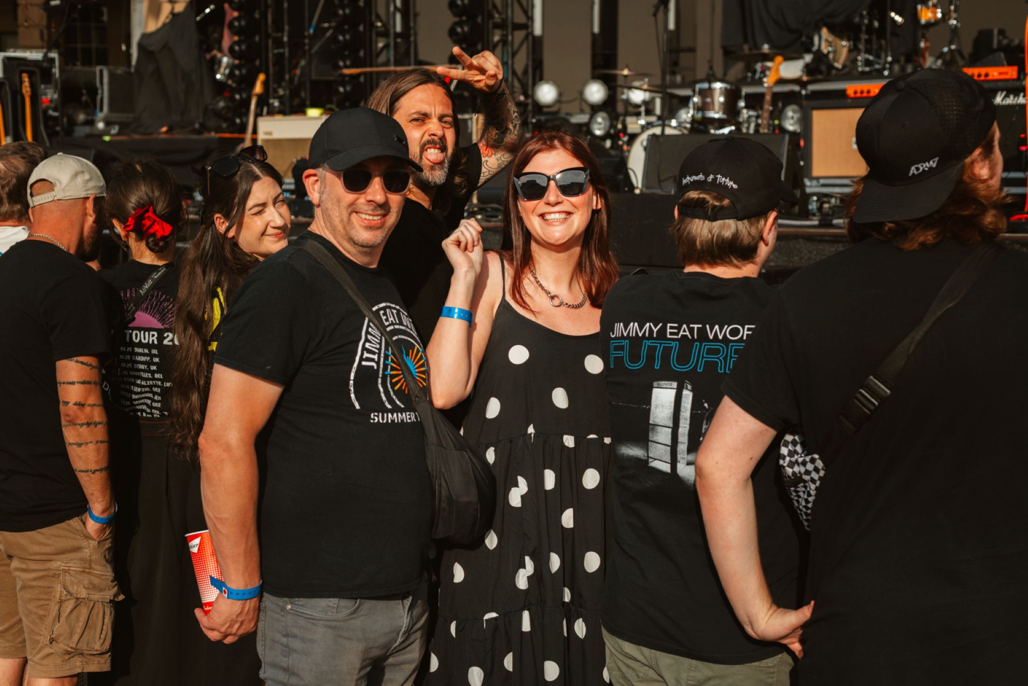 Festival-goers in casual attire smiling near a concert stage
