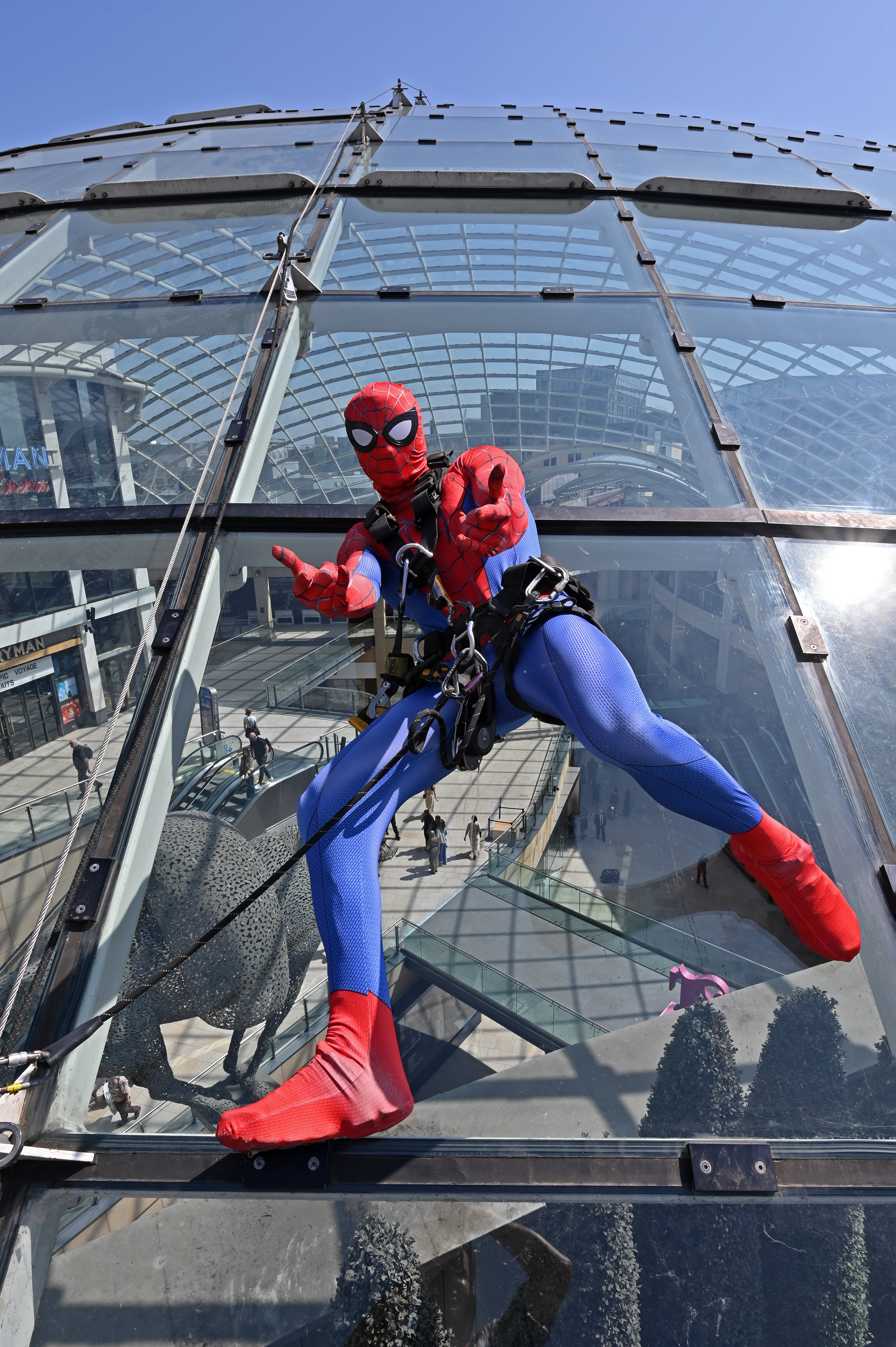 Person in superhero costume abseiling down glass building