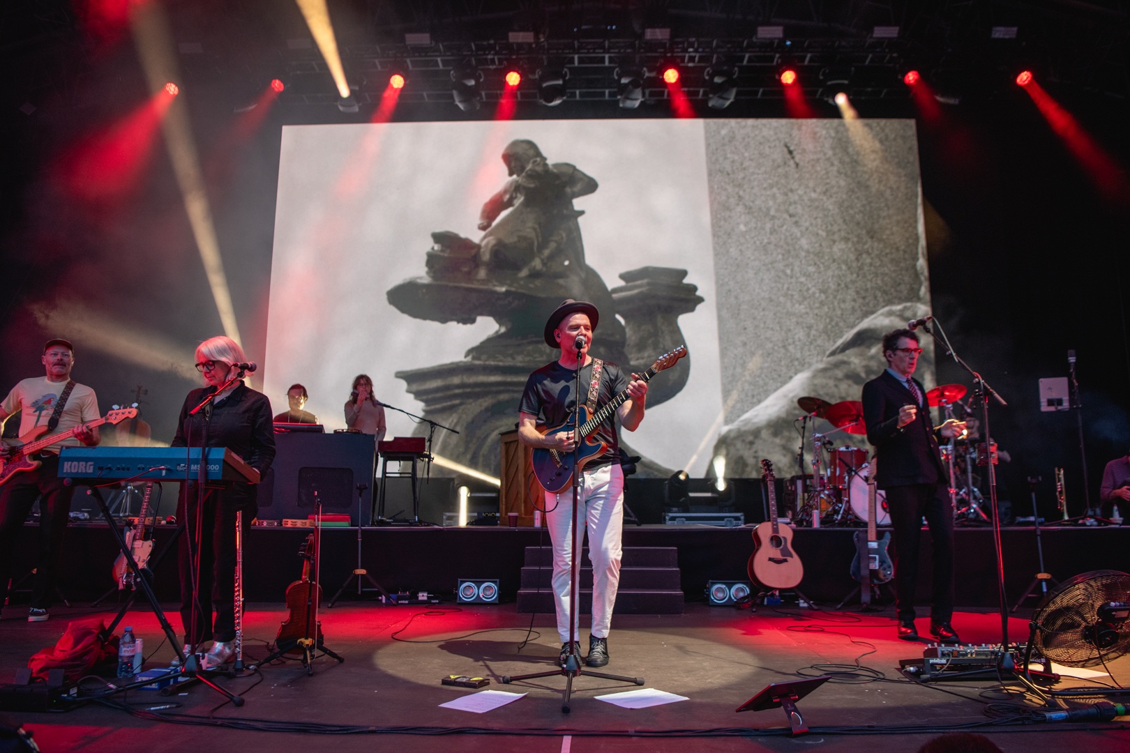 Band performing on stage with large screen backdrop and colorful lights