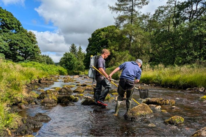 Two people in waders exploring a rocky stream in a green forest
