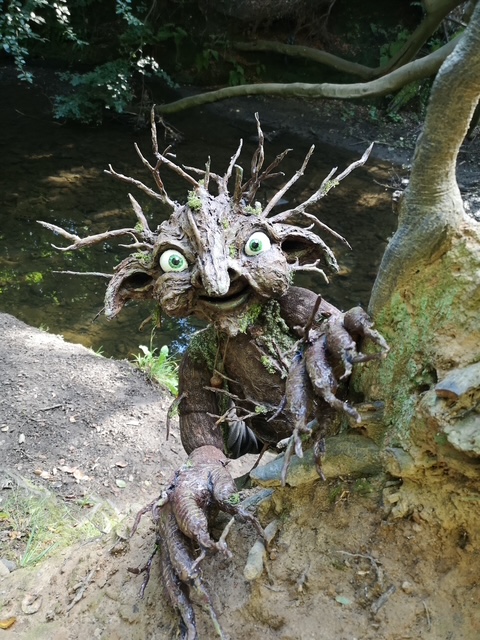 Whimsical tree creature with twig hair by a woodland stream