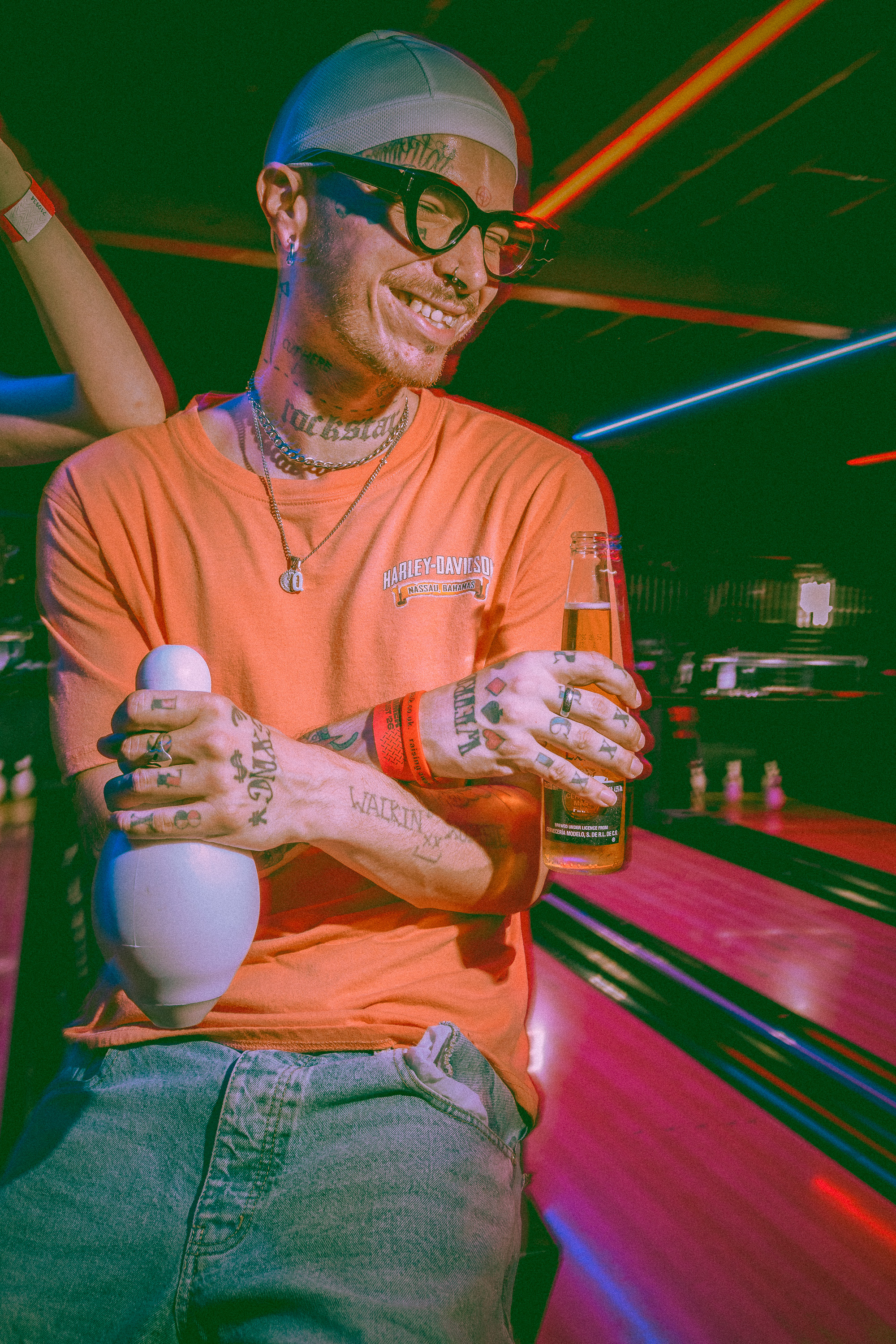 Man with tattoos and glasses holding bowling pin and drink