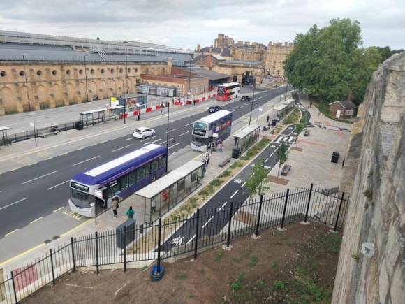 Buses and pedestrians on a street beside historic York city walls