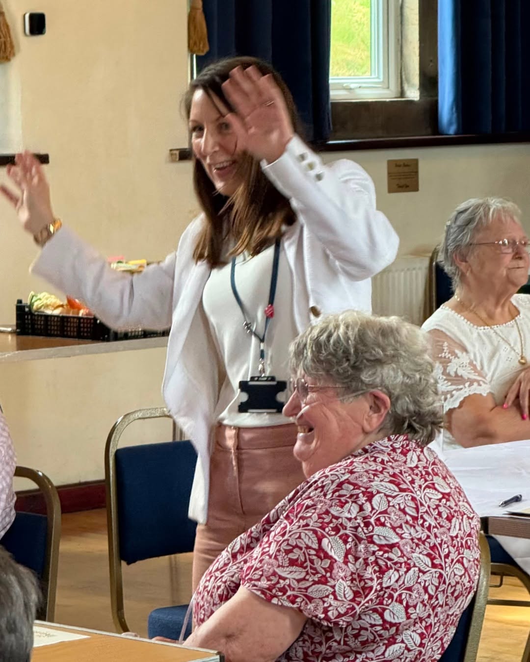 Smiling woman in white jacket engaging with seated seniors