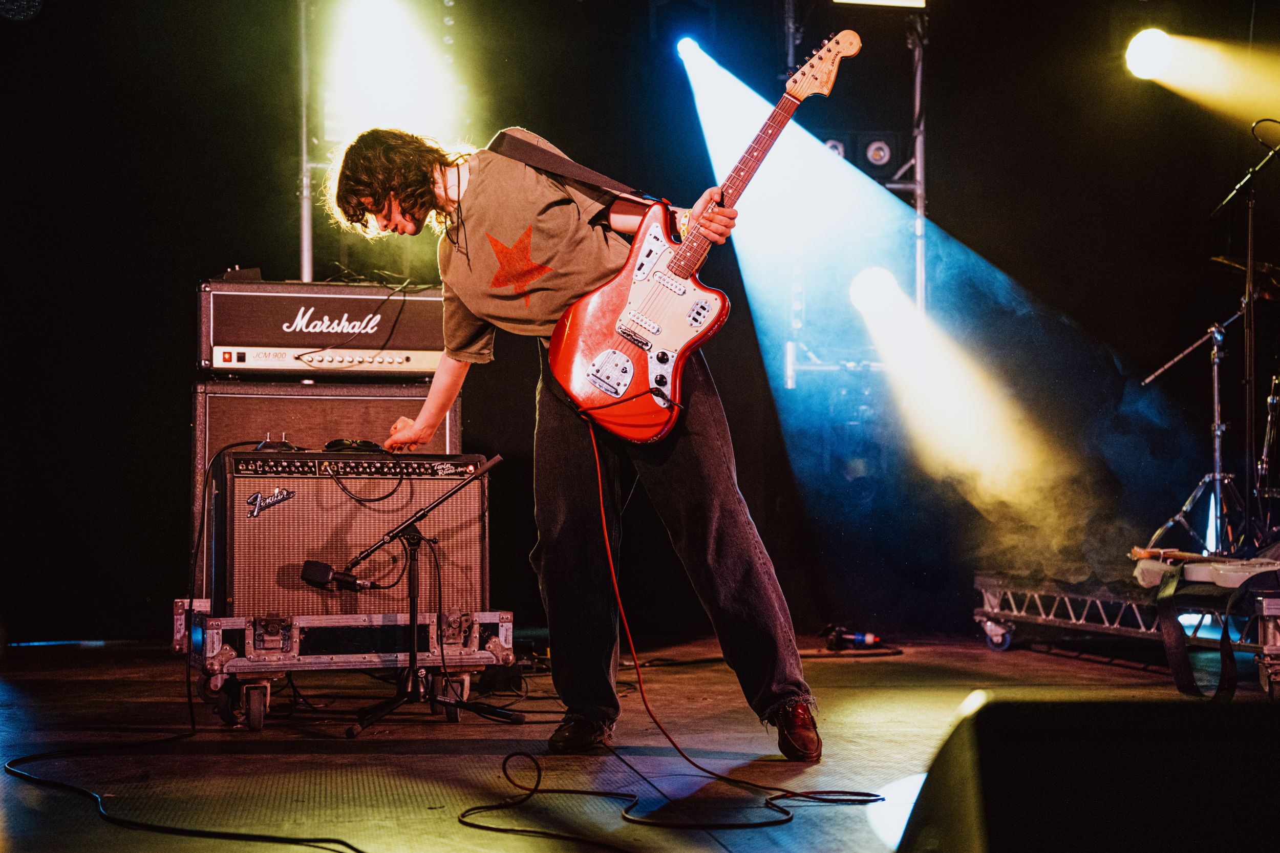 Guitarist on stage adjusting amplifier with vibrant lights