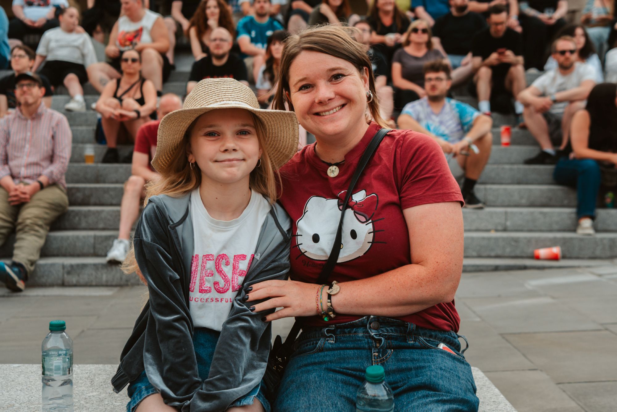 Mother and daughter smiling on stone steps with crowd behind