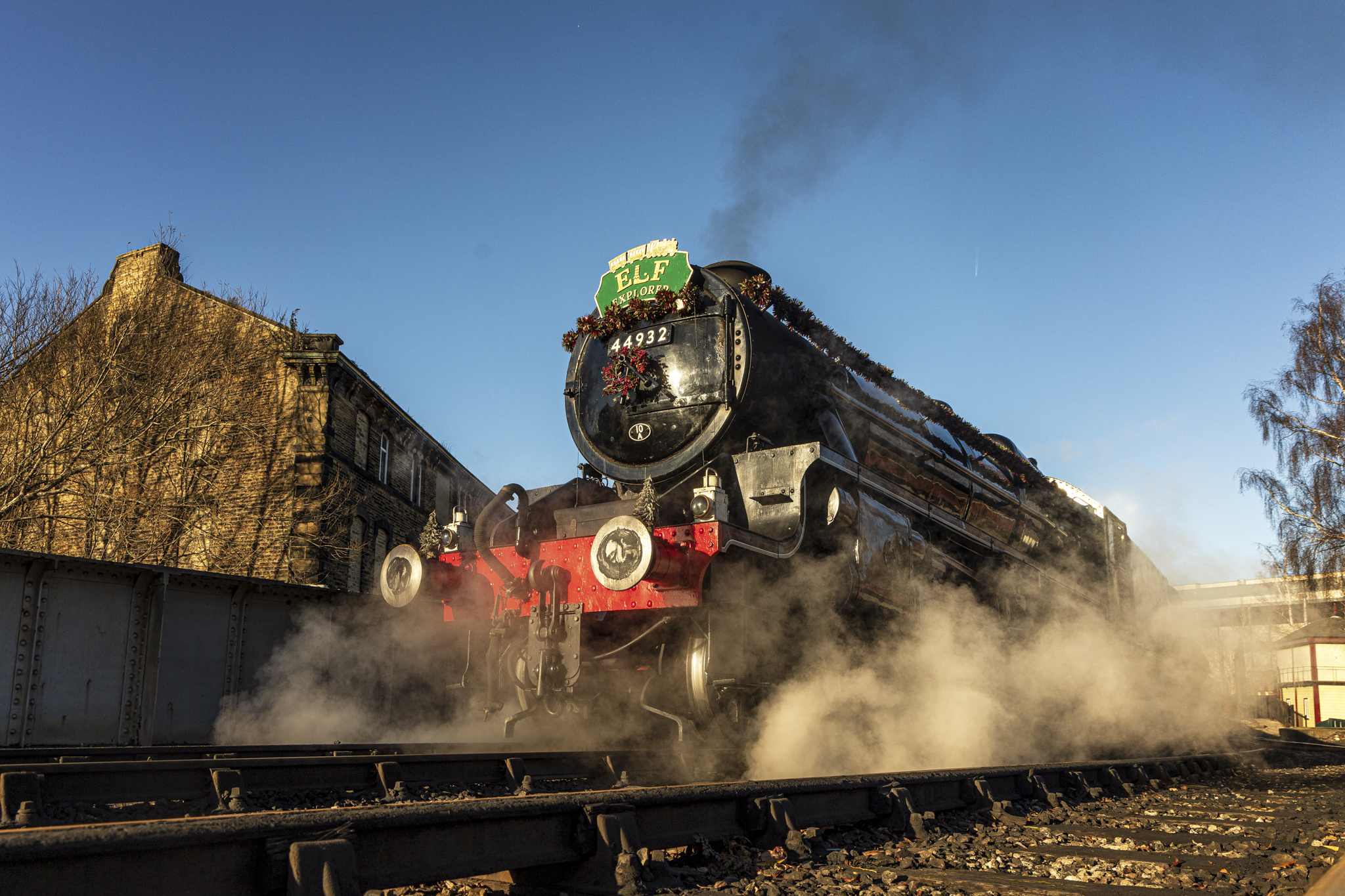 Steam train decorated for Christmas on tracks beside a stone building