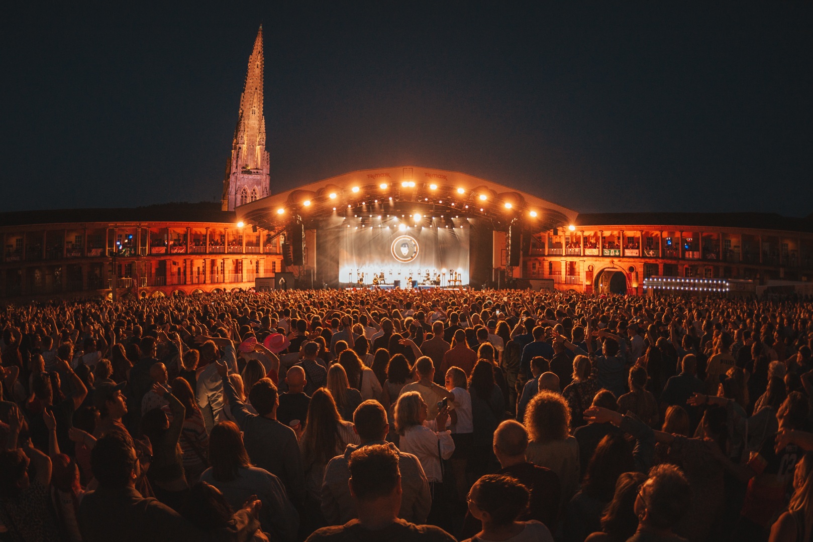 Crowd at an outdoor concert at night with illuminated stage