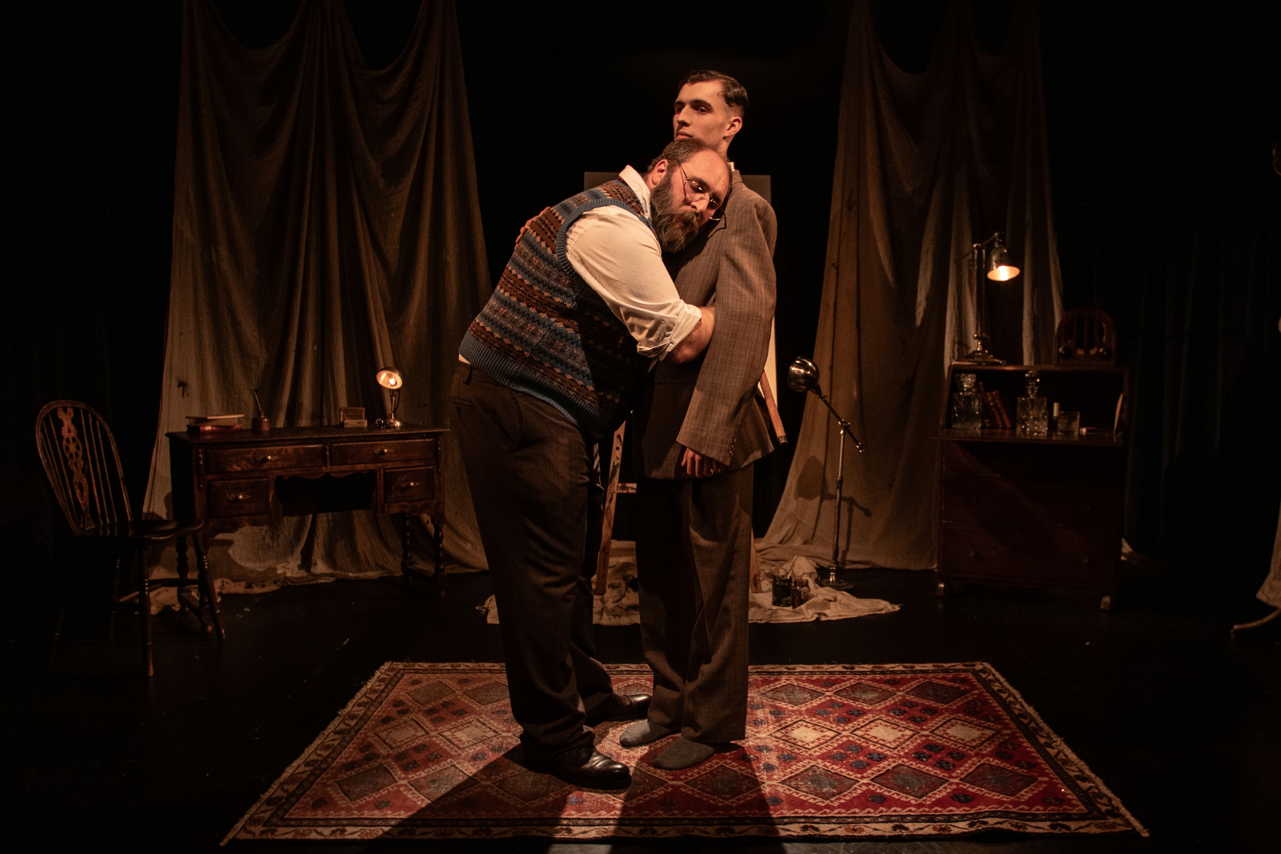 Two men in vintage suits embracing on a dimly lit stage