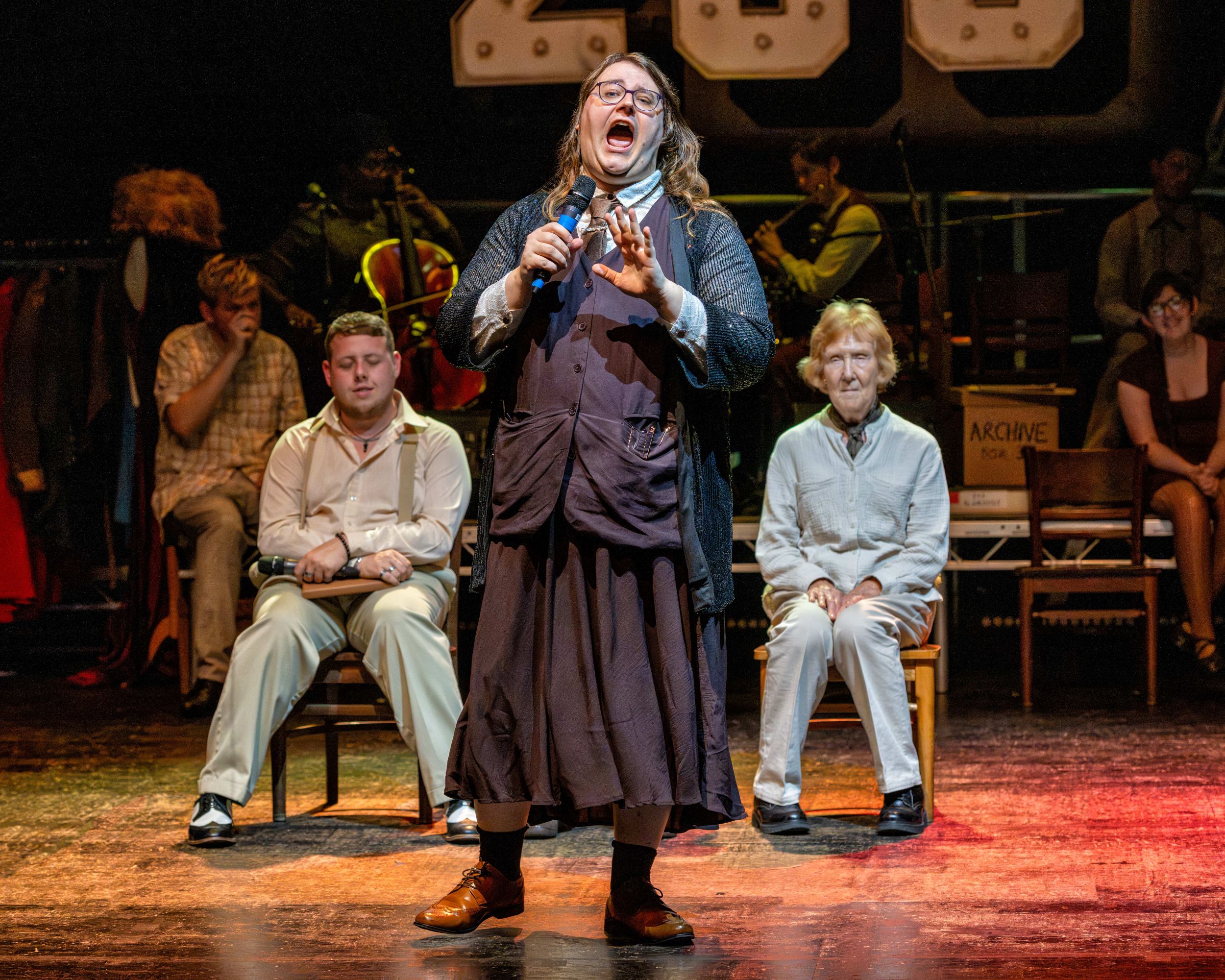 Woman singing passionately on stage with audience seated behind