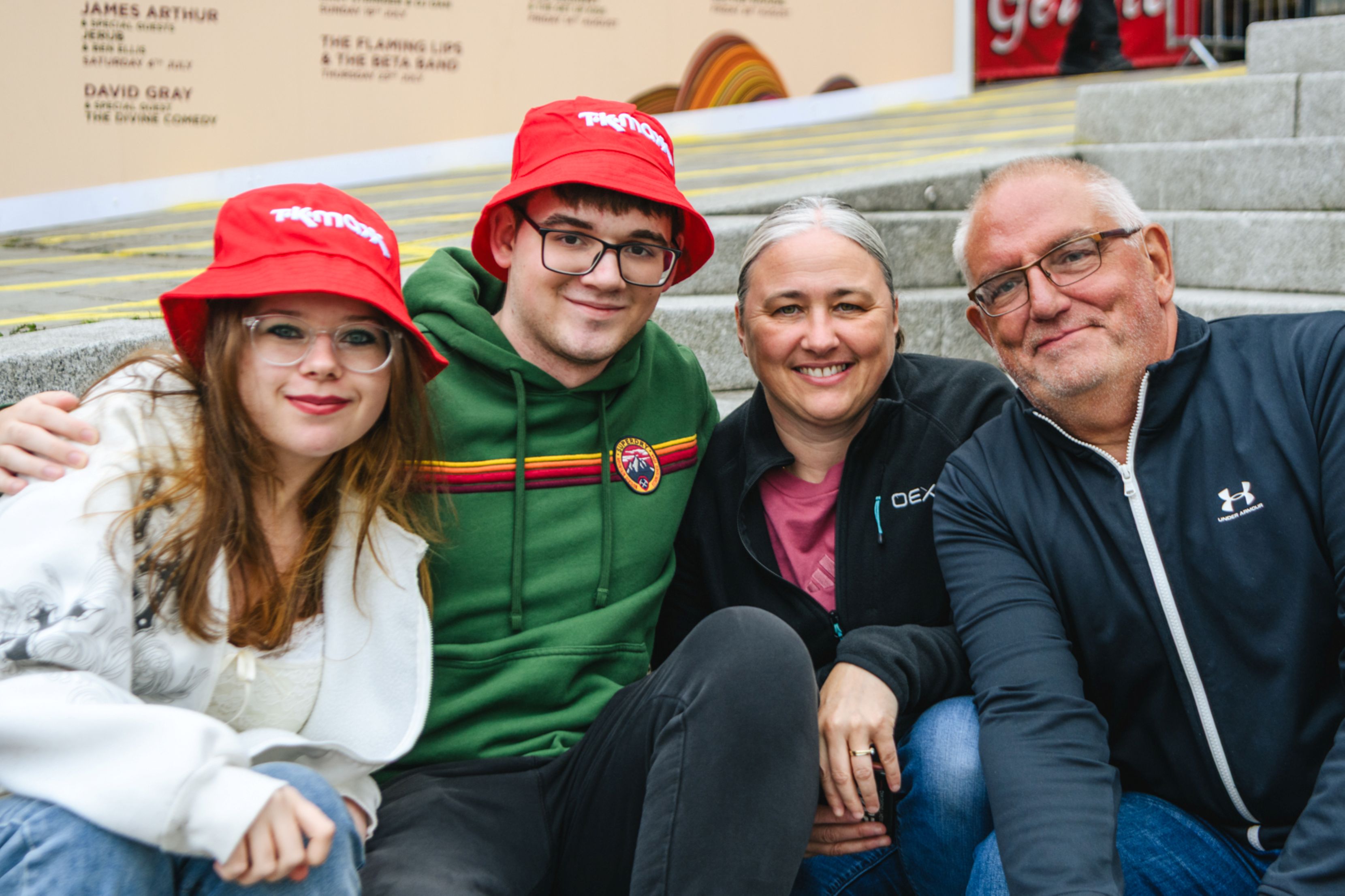 Group of four people sitting on stone steps wearing casual clothes and red hats