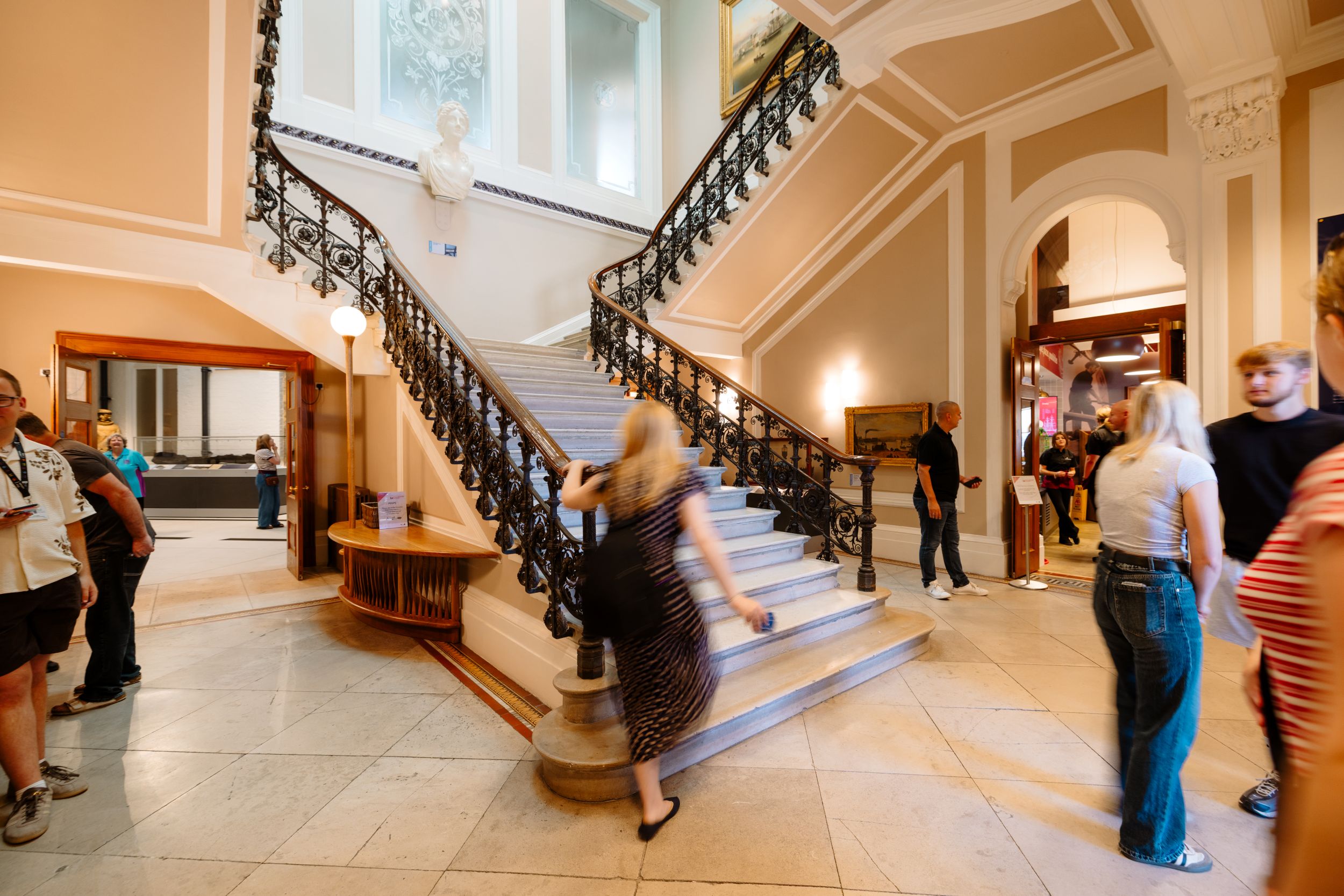Visitors in grand staircase area with ornate railings and bust