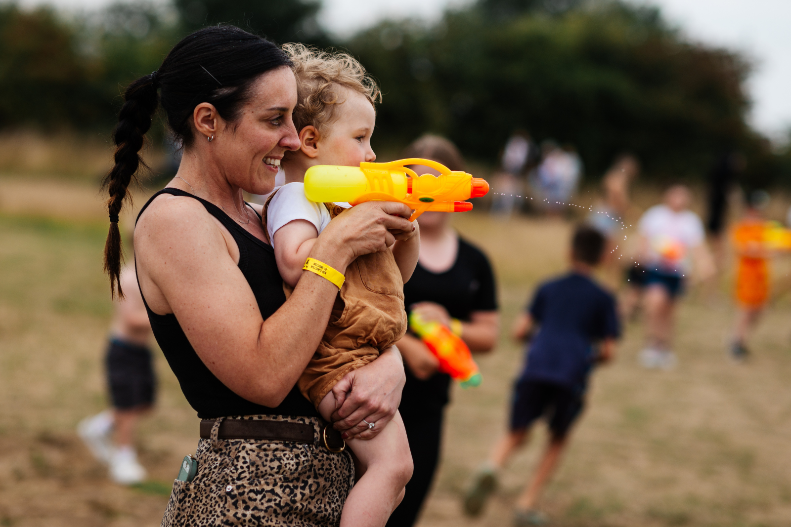 Mother holding toddler with water pistol in countryside park
