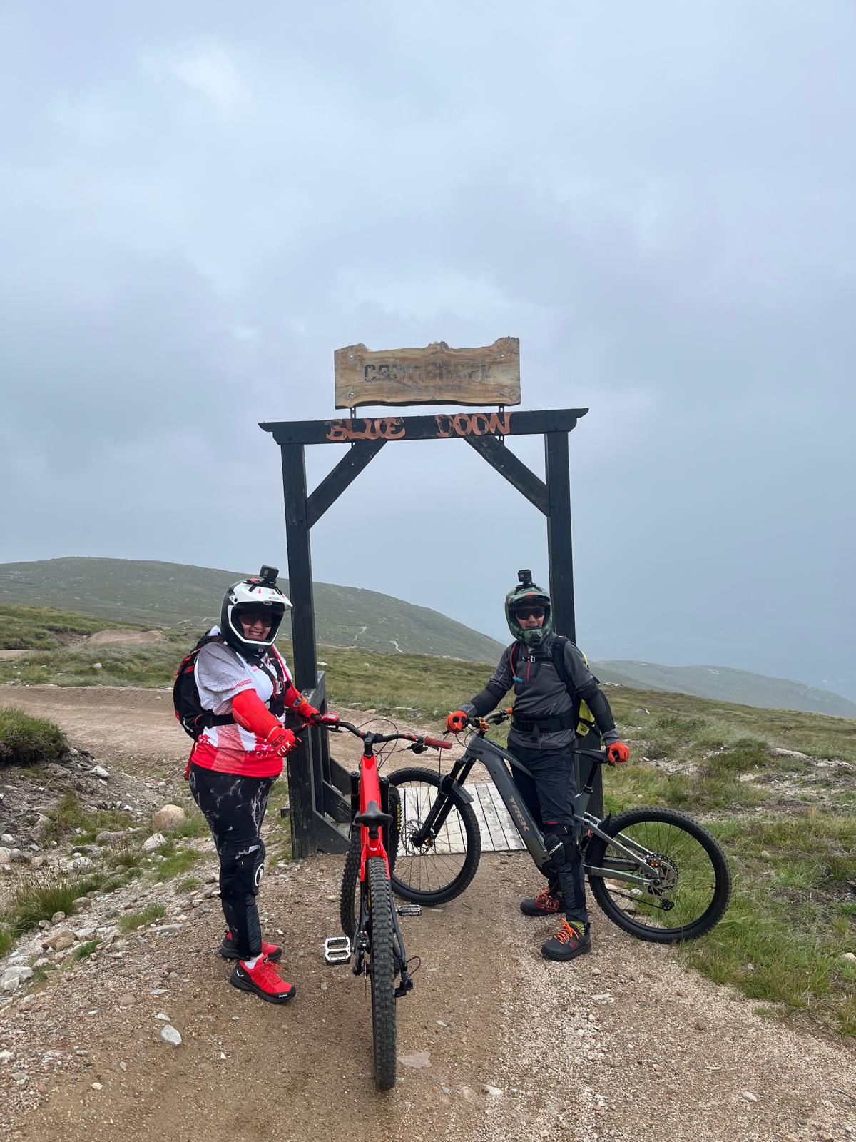 Cyclists in protective gear at mountain trail gate under cloudy sky