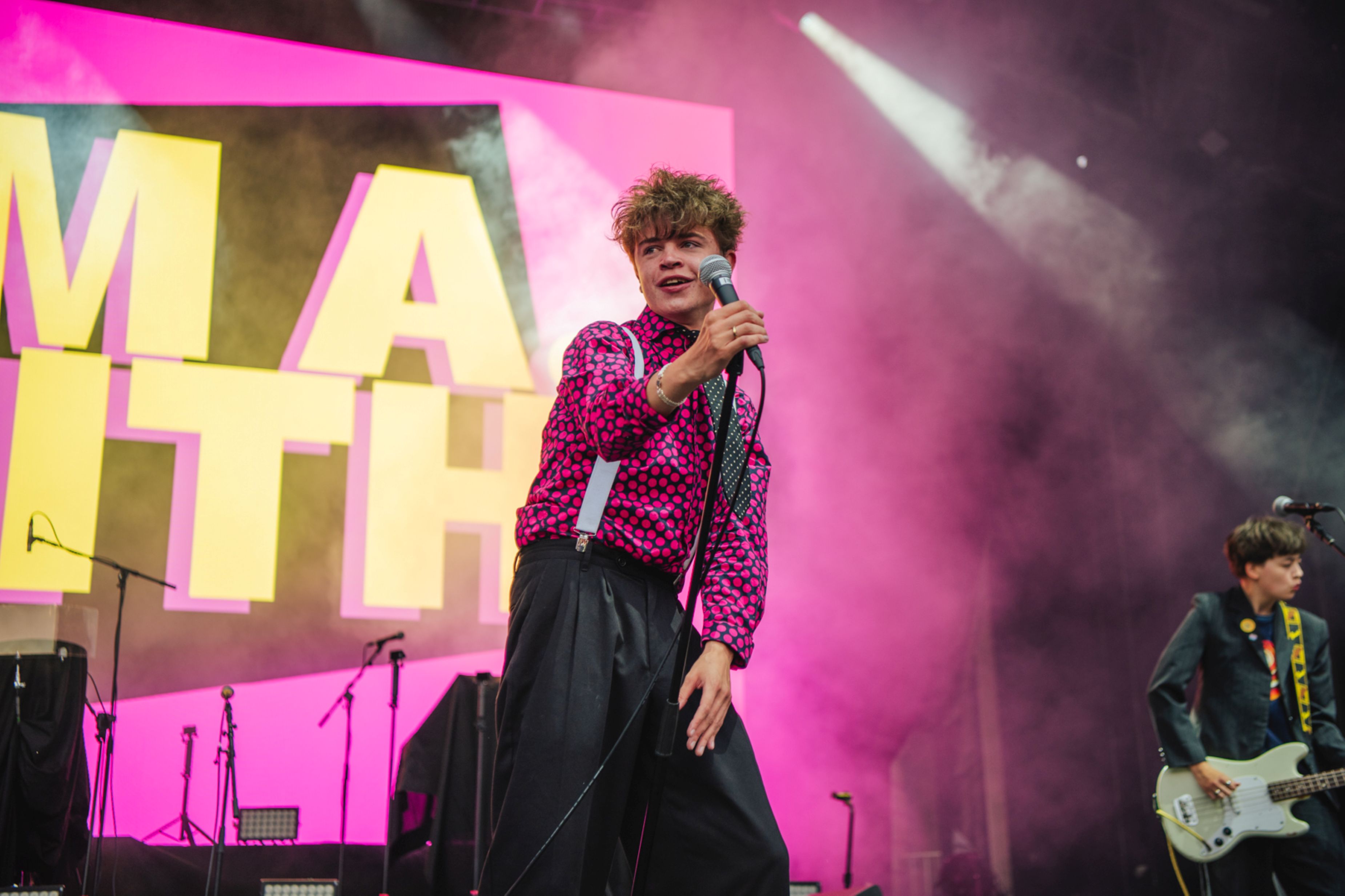 Young male singer in pink shirt performs on stage with vibrant lights