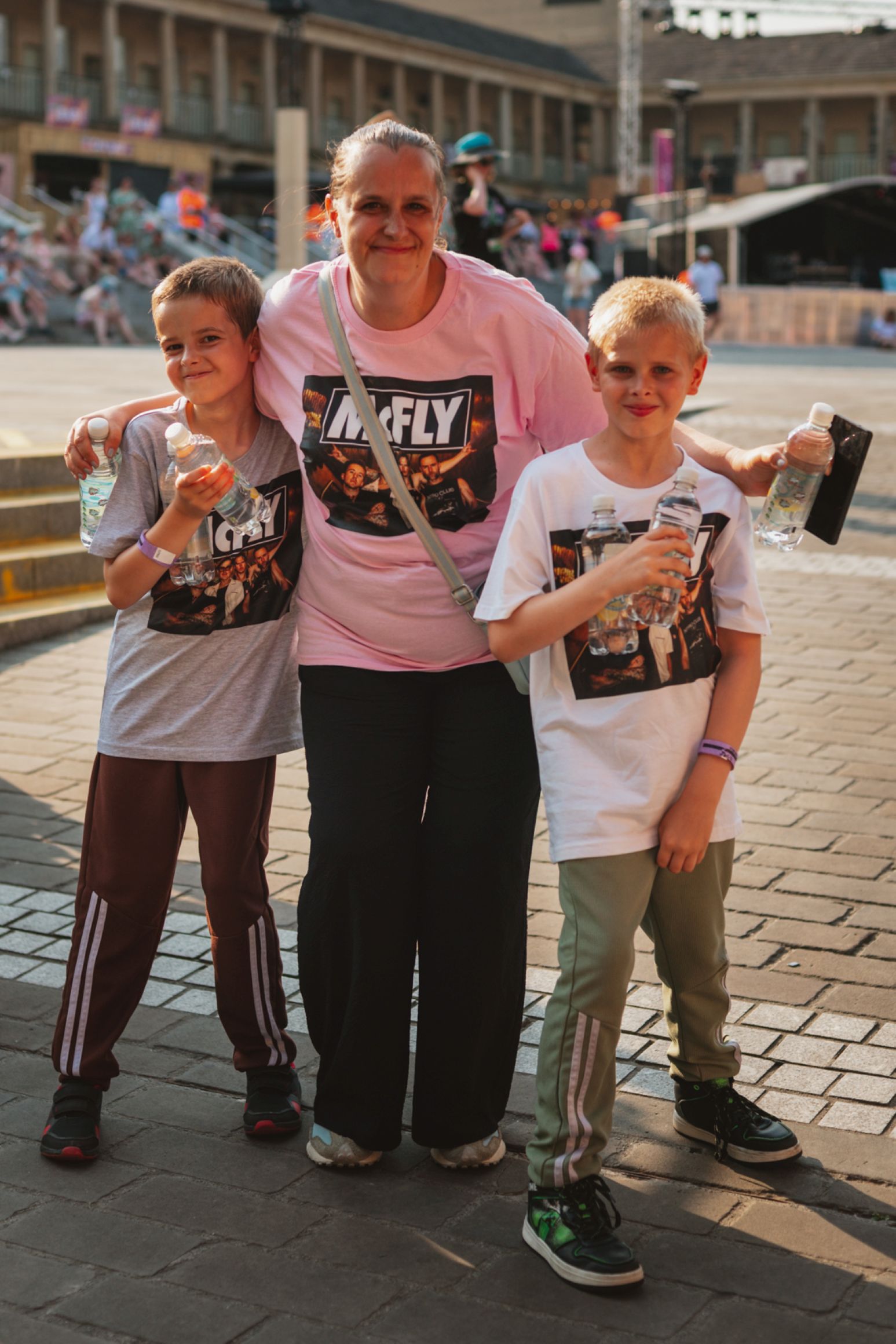 Smiling woman with two boys holding water bottles at outdoor event