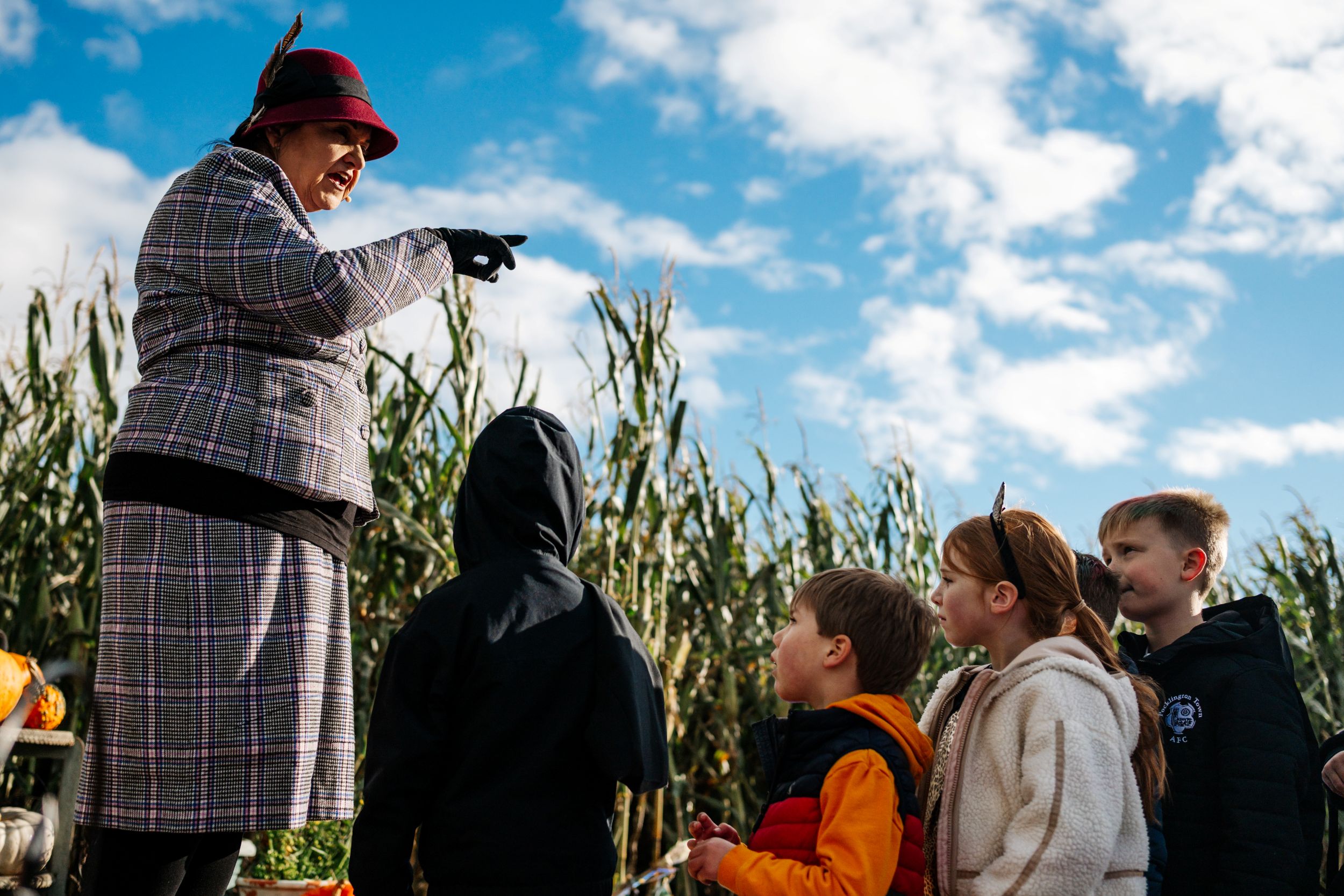 Woman in hat and coat talking to children in a cornfield