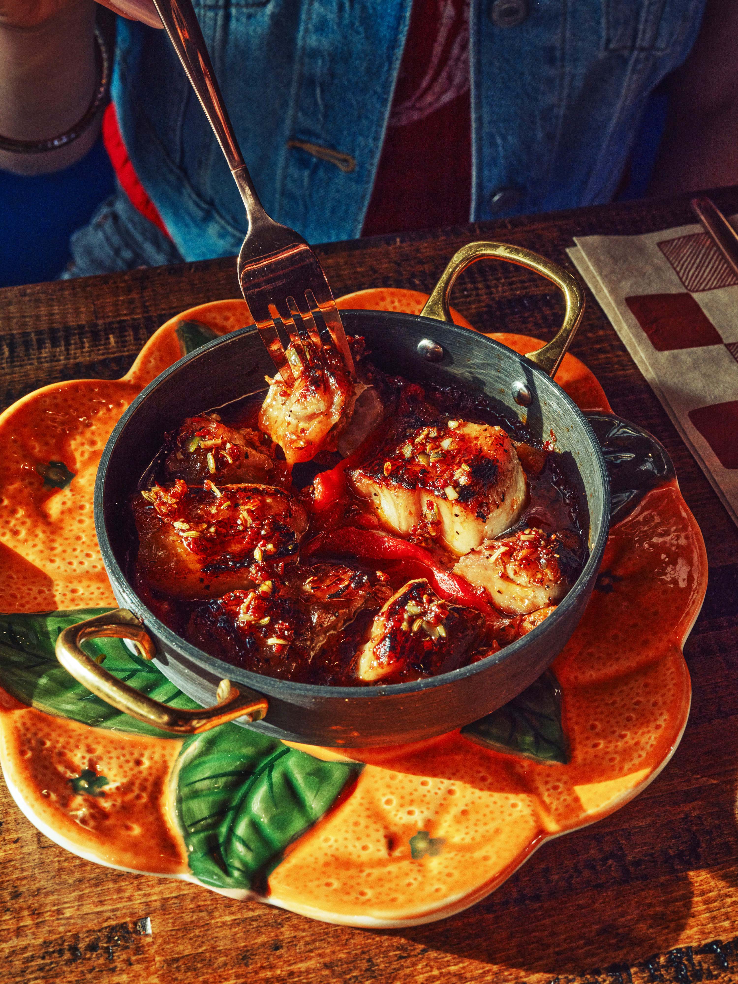 Person eating sizzling garlic prawns in cast iron dish