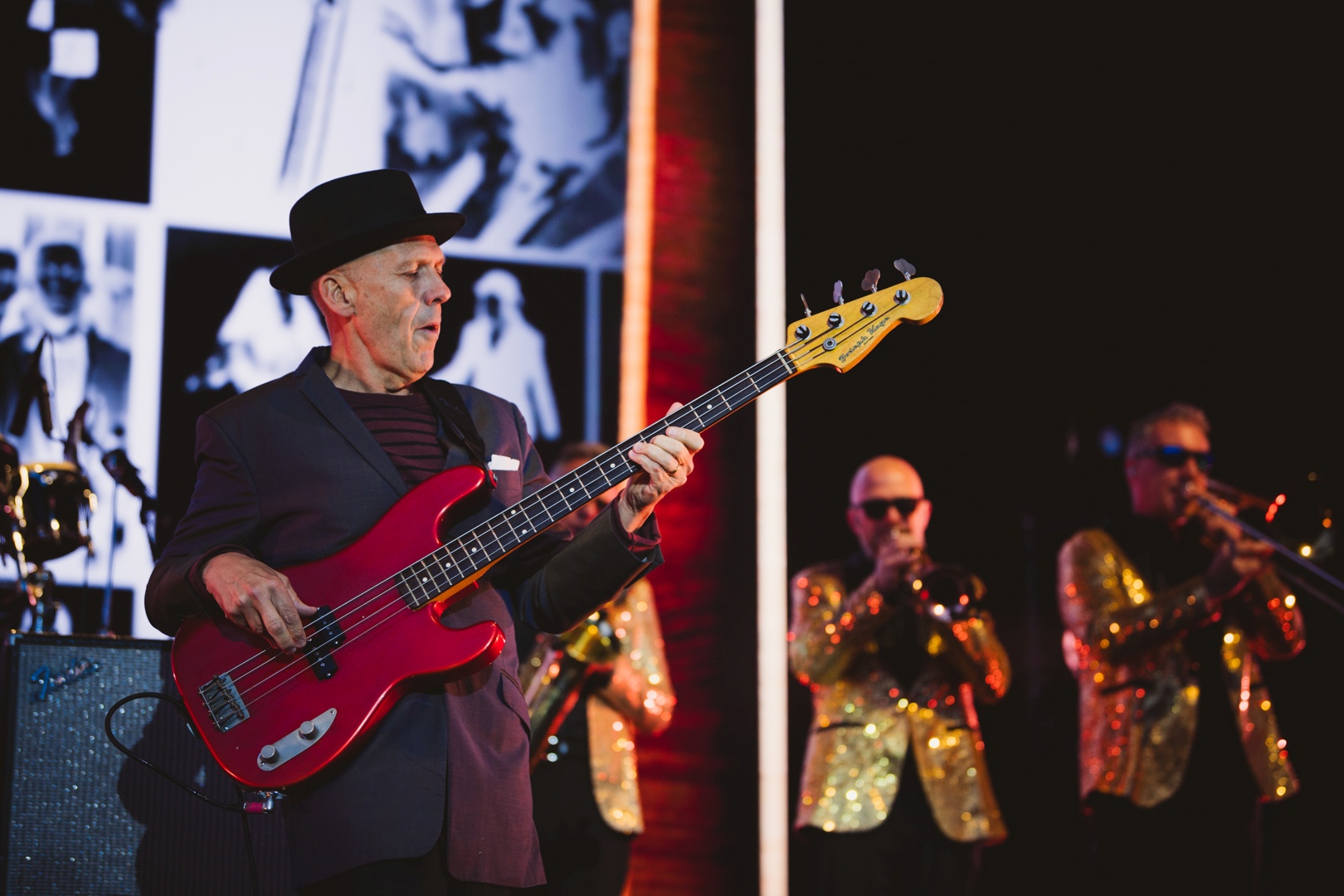 Musician playing bass guitar on stage with brass band
