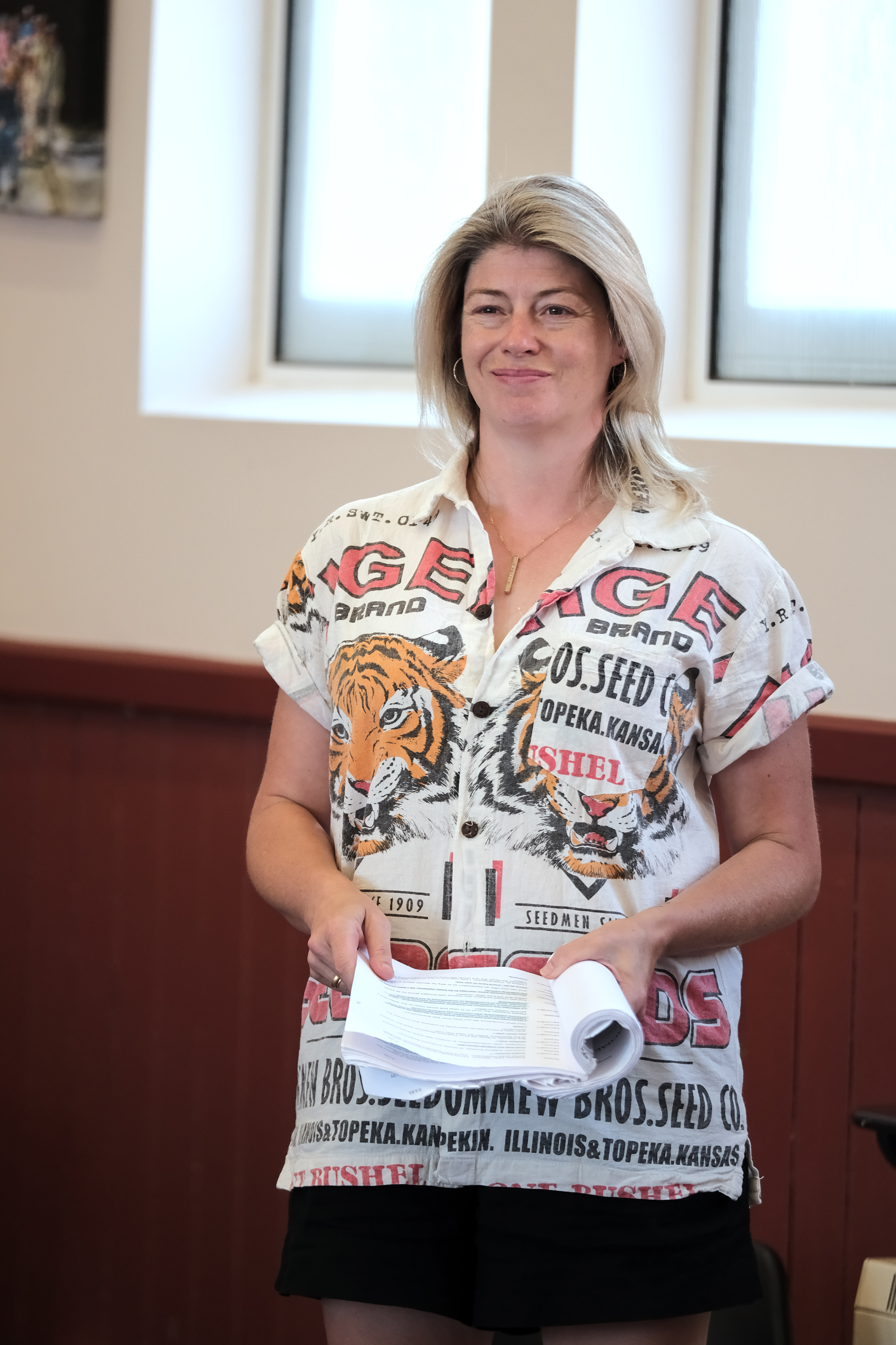 Smiling woman in a graphic shirt holding papers indoors