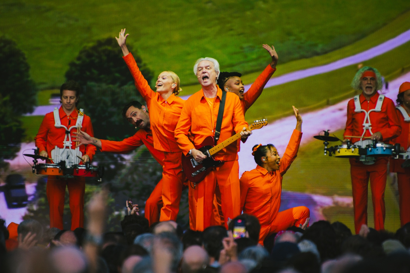 Performers in bright orange outfits playing instruments on stage