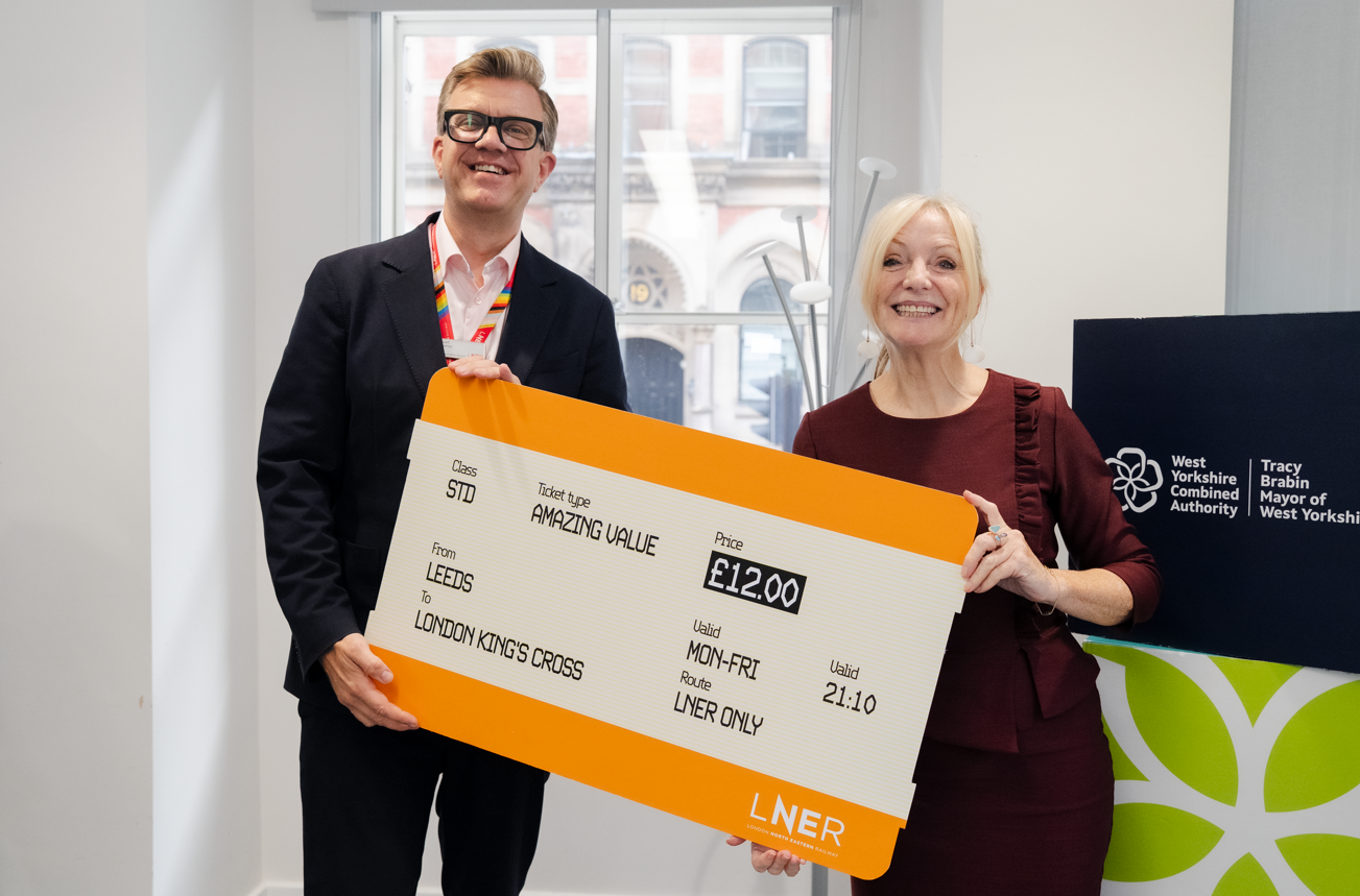 Two people smiling holding a large novelty train ticket indoors