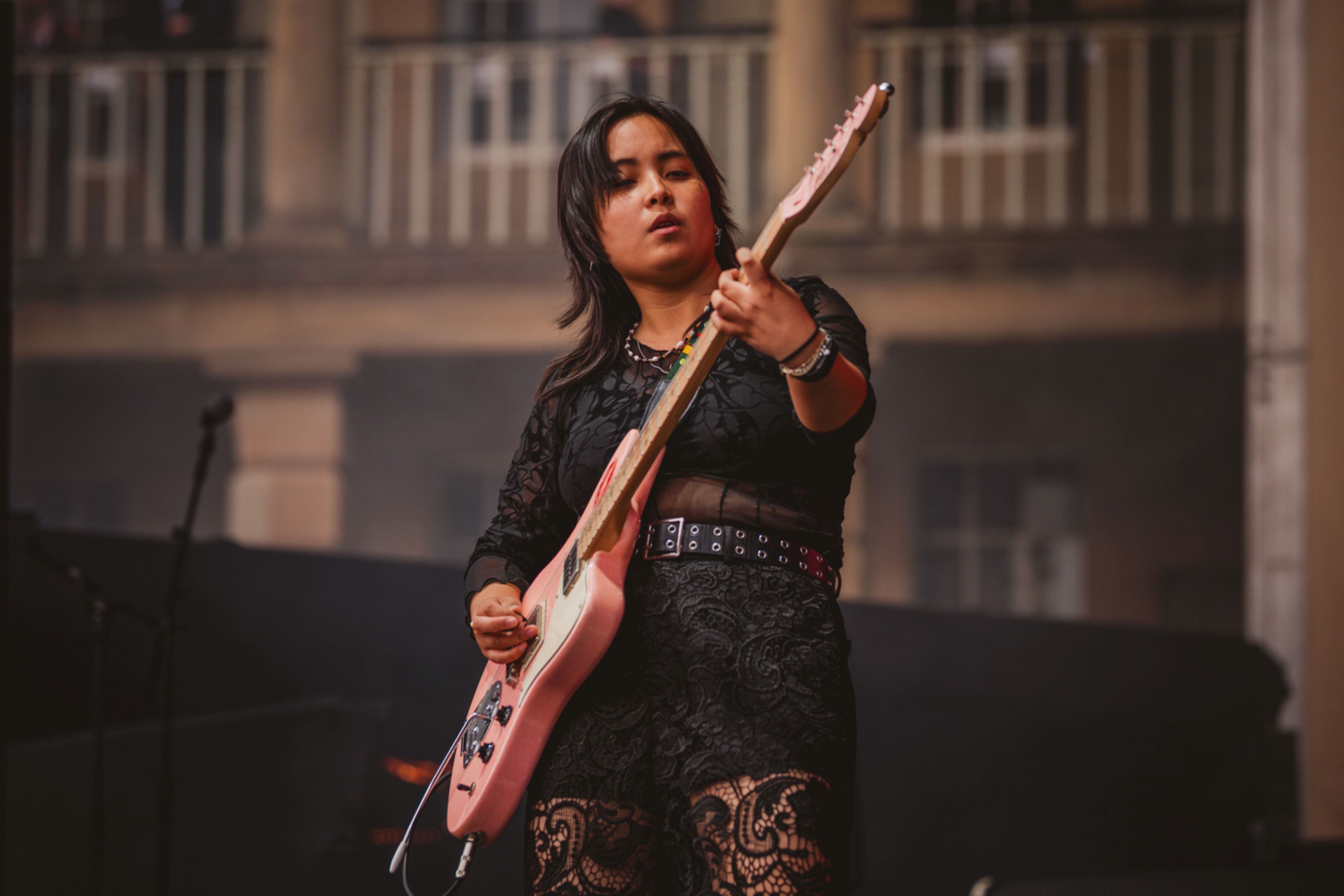 Musician playing electric guitar on stage with historic building backdrop