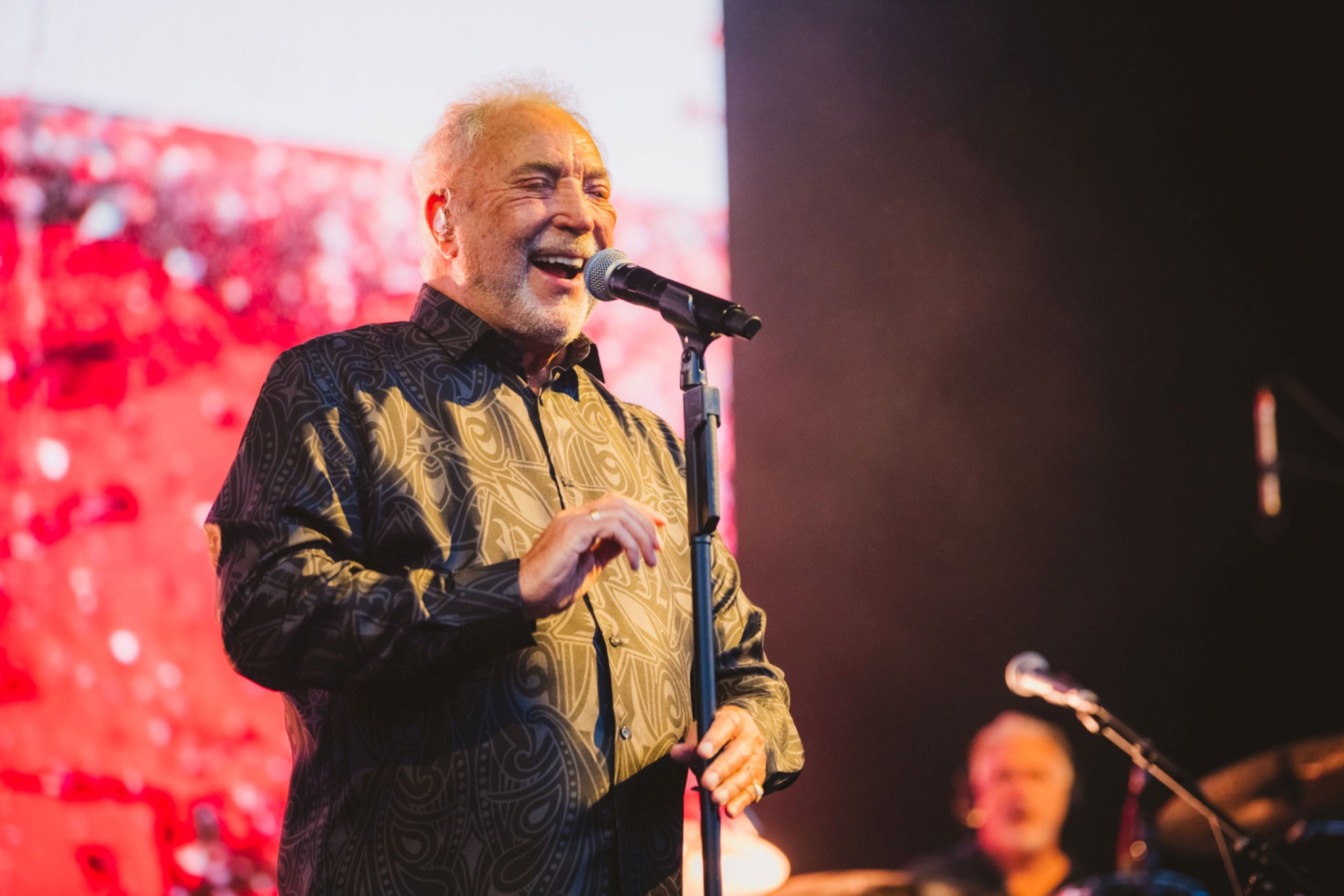 Elderly man in patterned shirt singing on stage with microphone