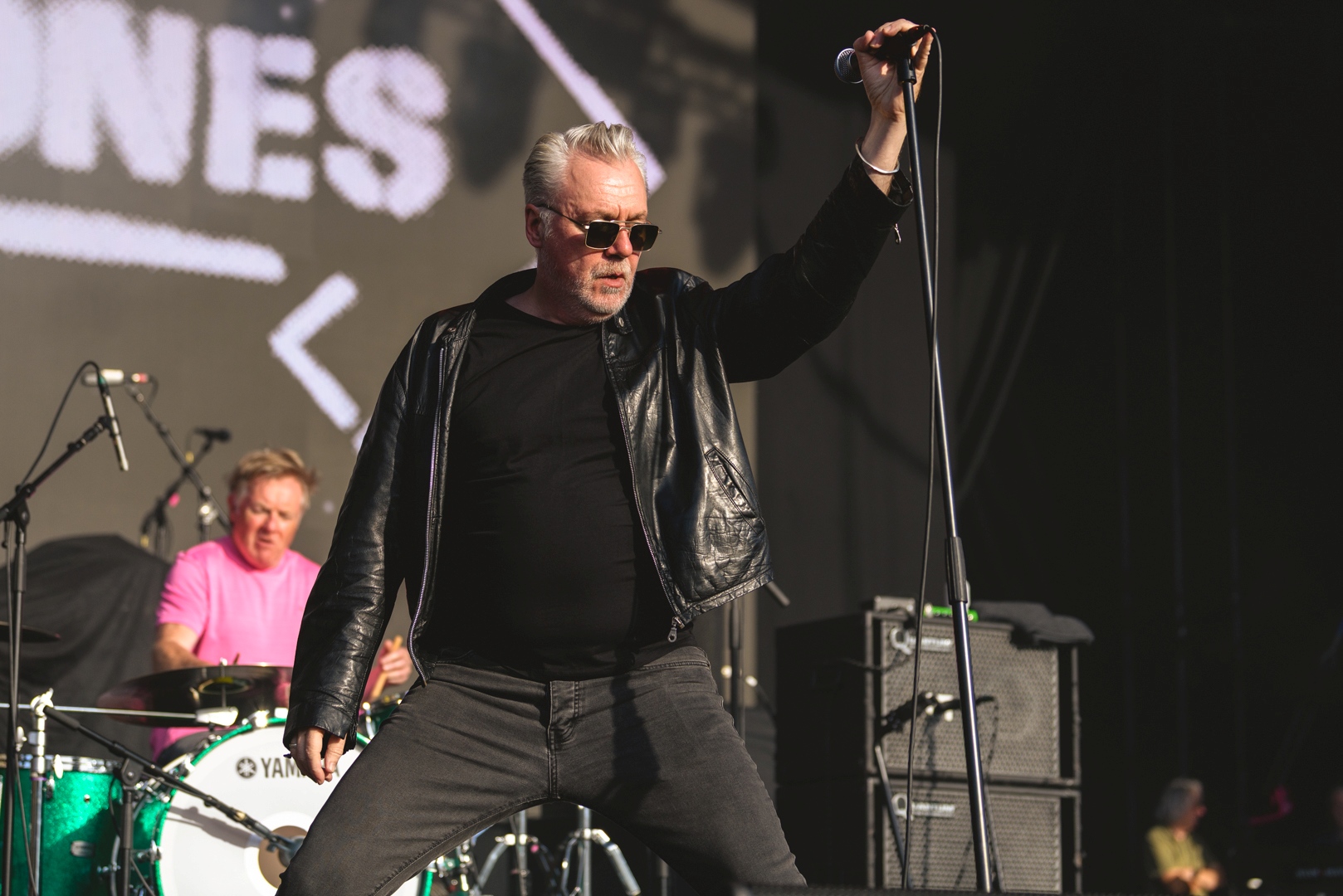 Musician in black leather jacket performing energetically on stage