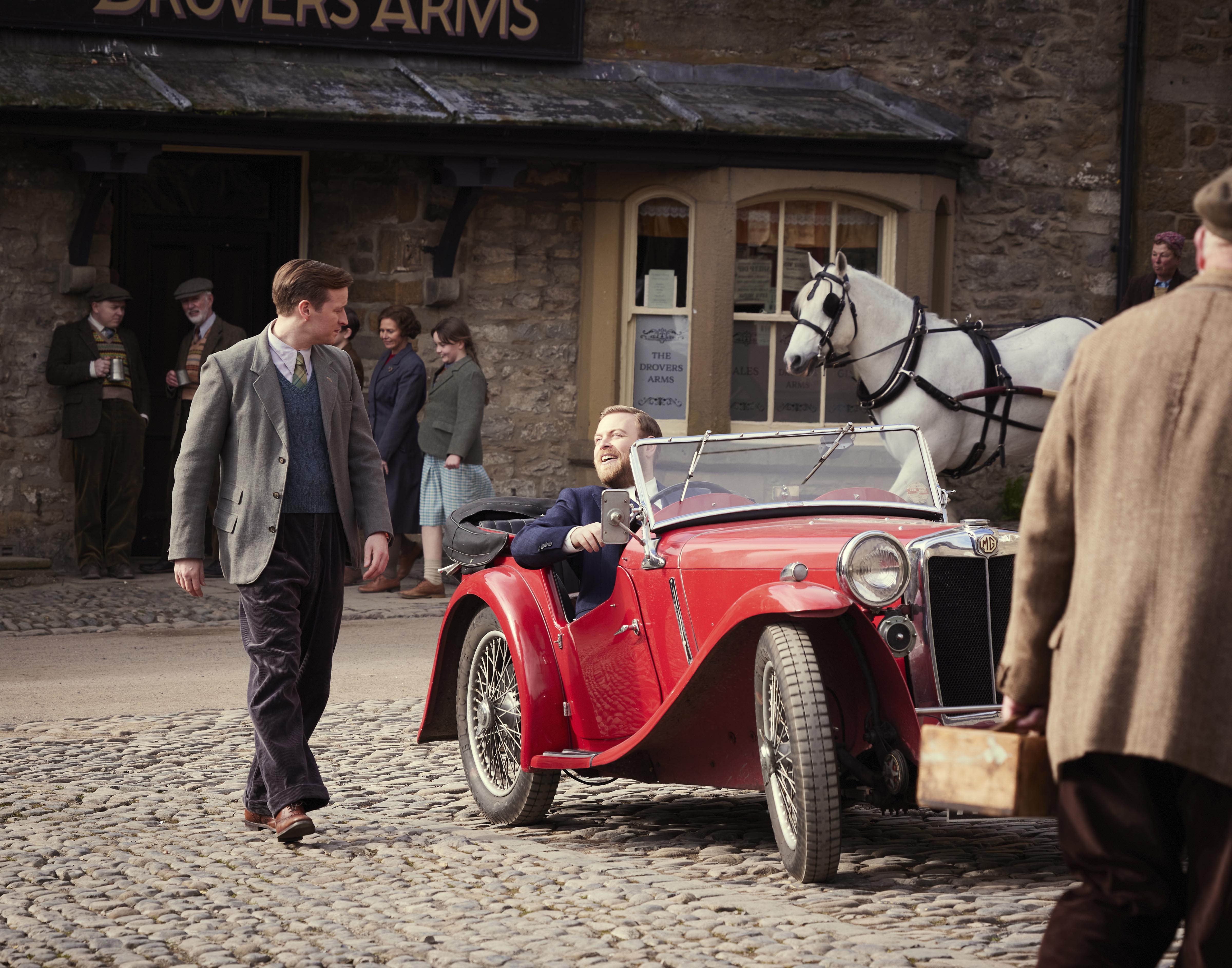 Vintage red convertible on cobblestone street with stone pub backdrop
