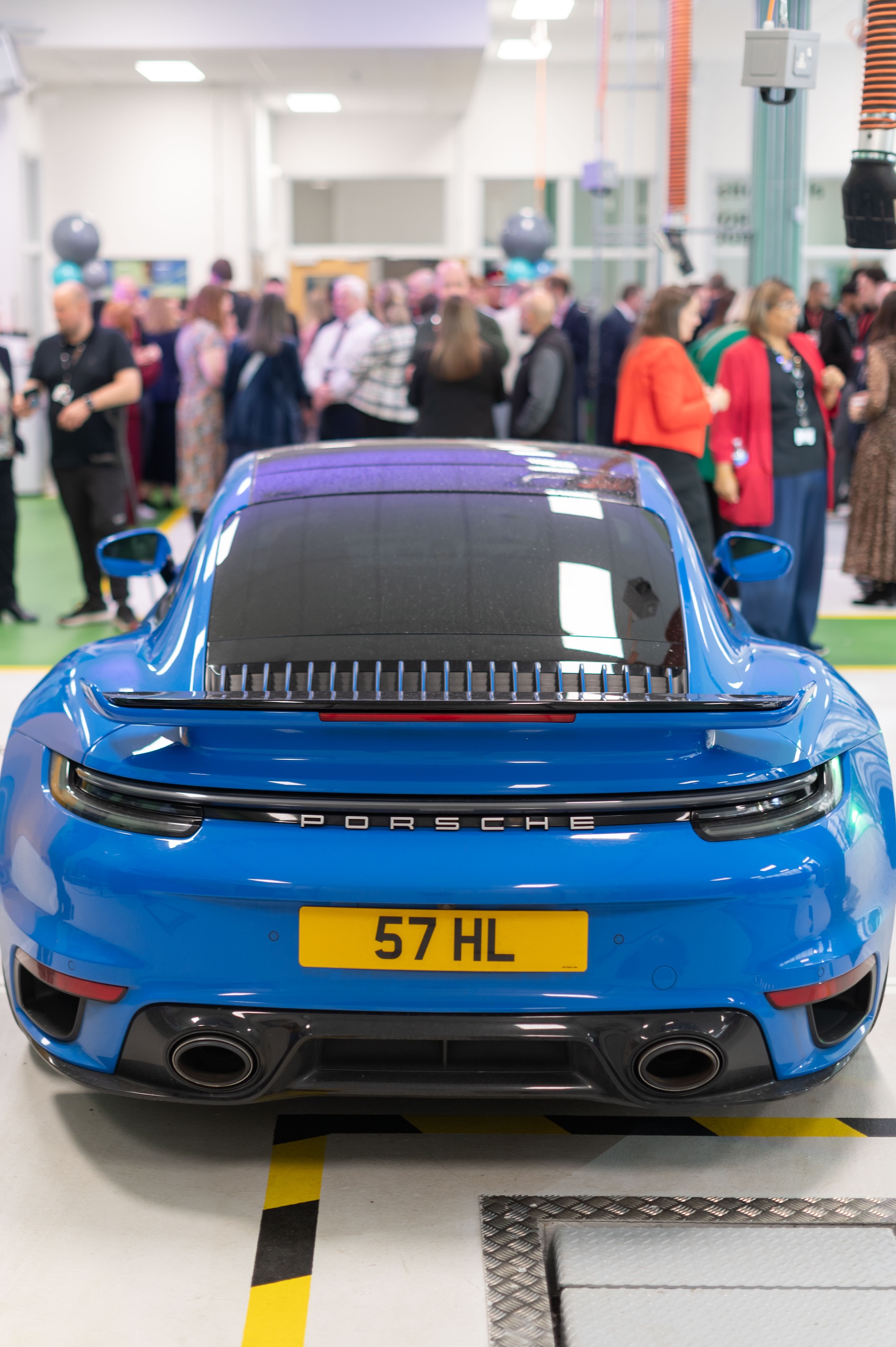 Blue Porsche sports car with crowd in modern showroom