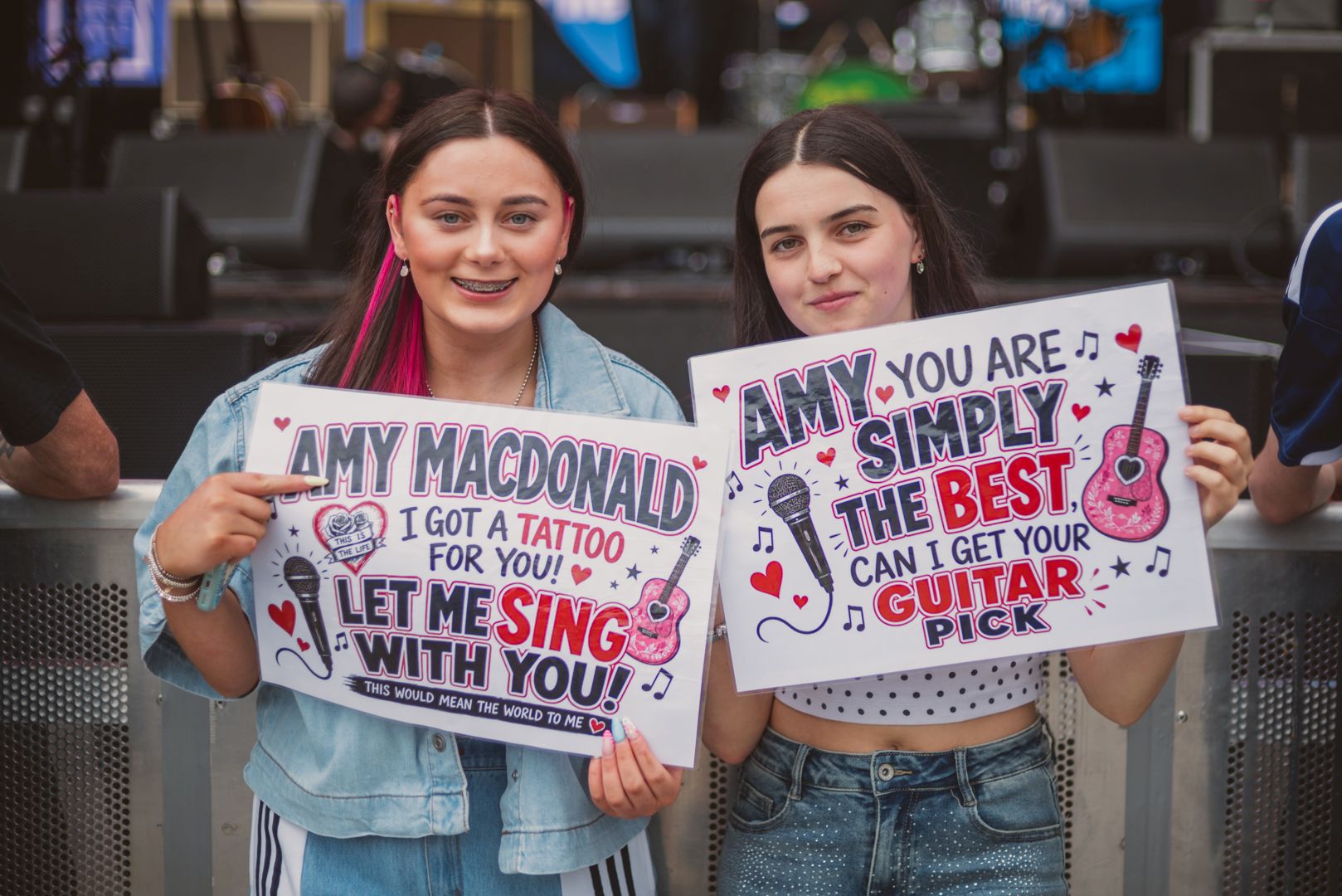 Two women holding colorful concert signs with guitars