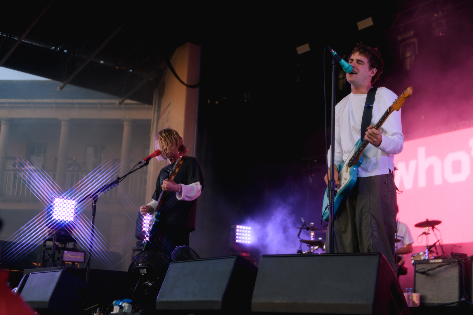 Two musicians performing on an outdoor stage with purple lighting