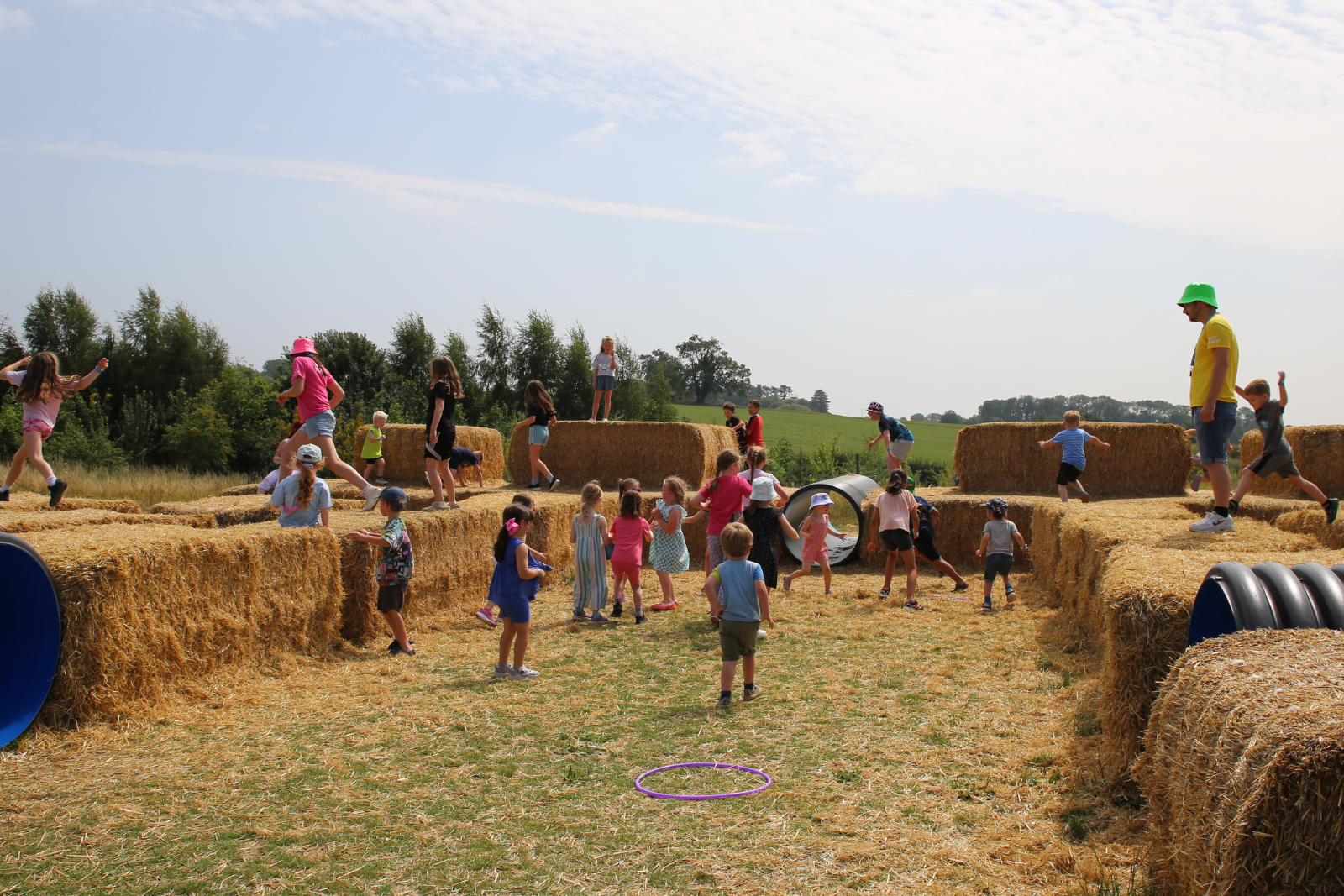 Children playing in a hay bale maze under a clear blue sky