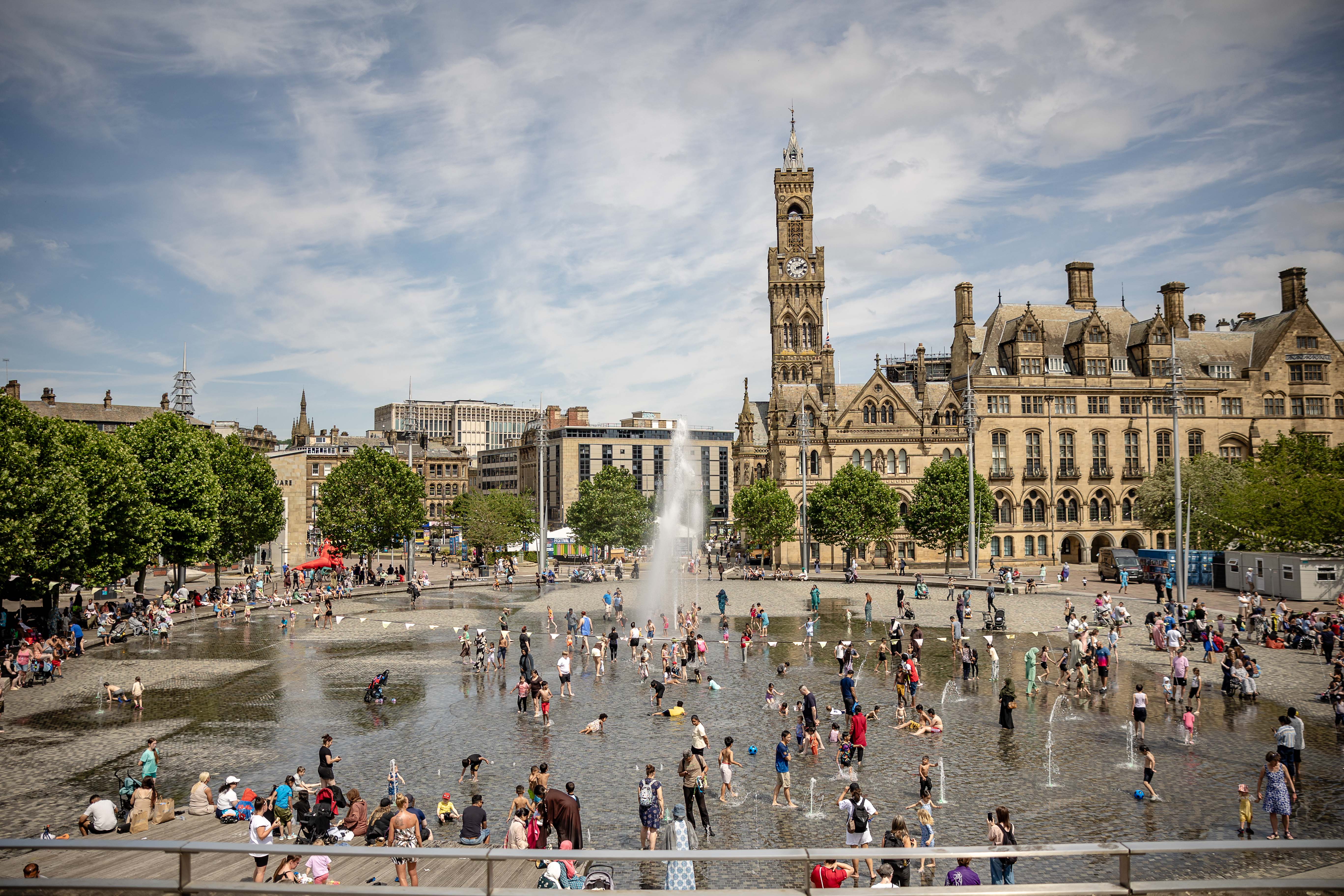 Families enjoying fountains in Bradford city park under blue sky