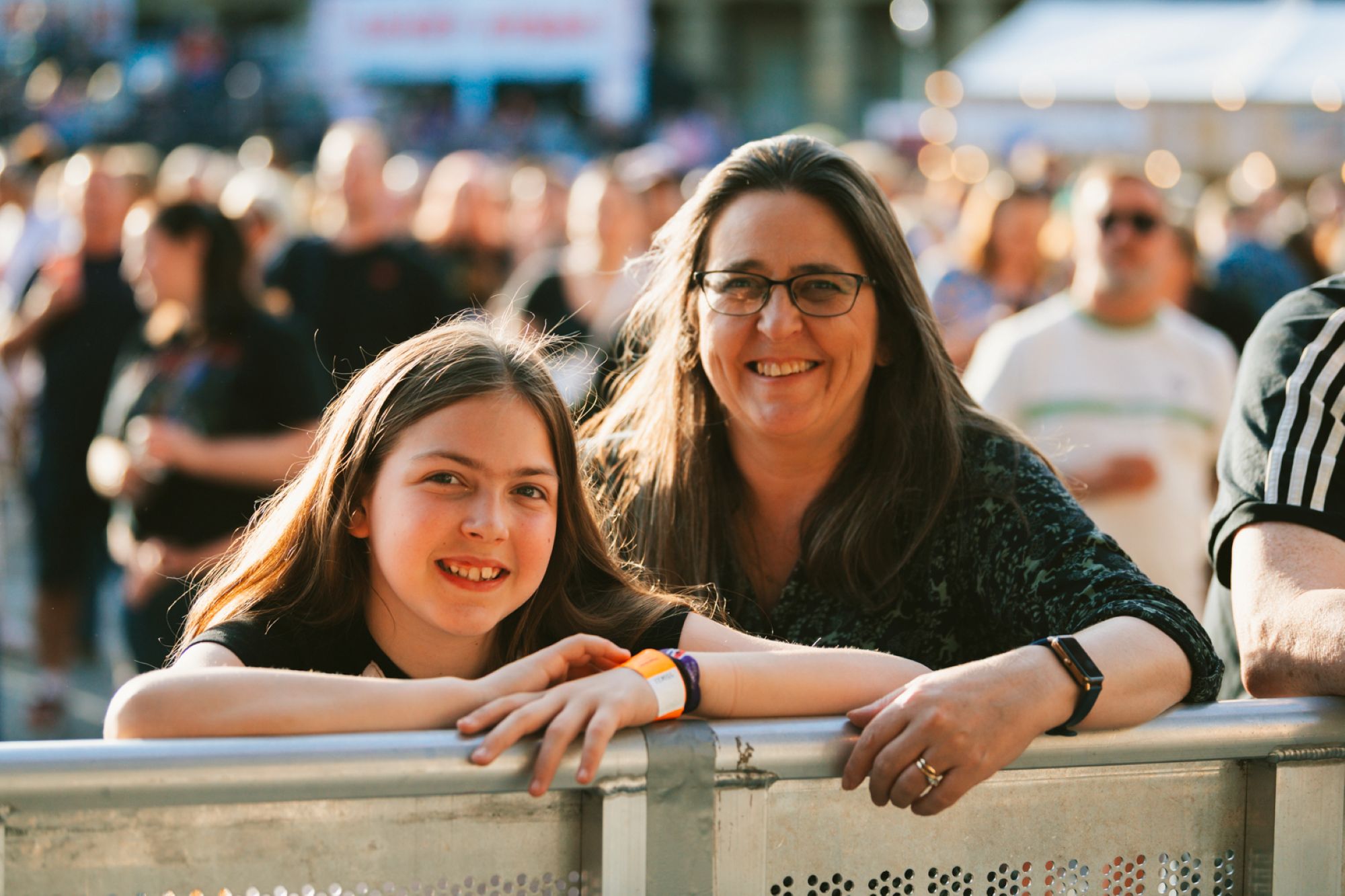 Smiling woman and girl leaning on metal barrier at outdoor event